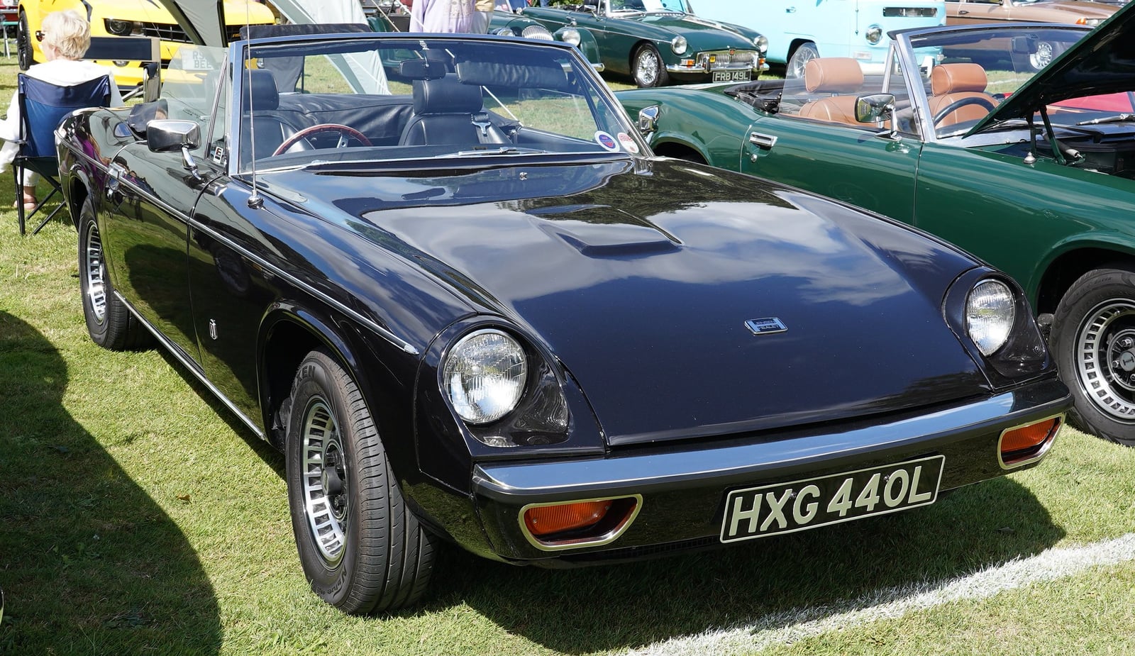 A dark Jensen-Healey roadster on grass at a show, front three-quarter view, UK registration HXG 440L