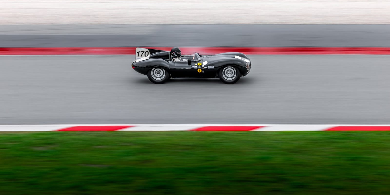 A black Jaguar D-Type racing car, number 170, at speed on a circuit