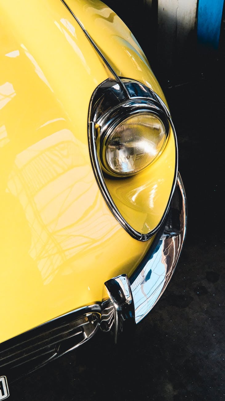 Close-up of the open headlamp and chrome bumper of a yellow Jaguar E-Type Series 2