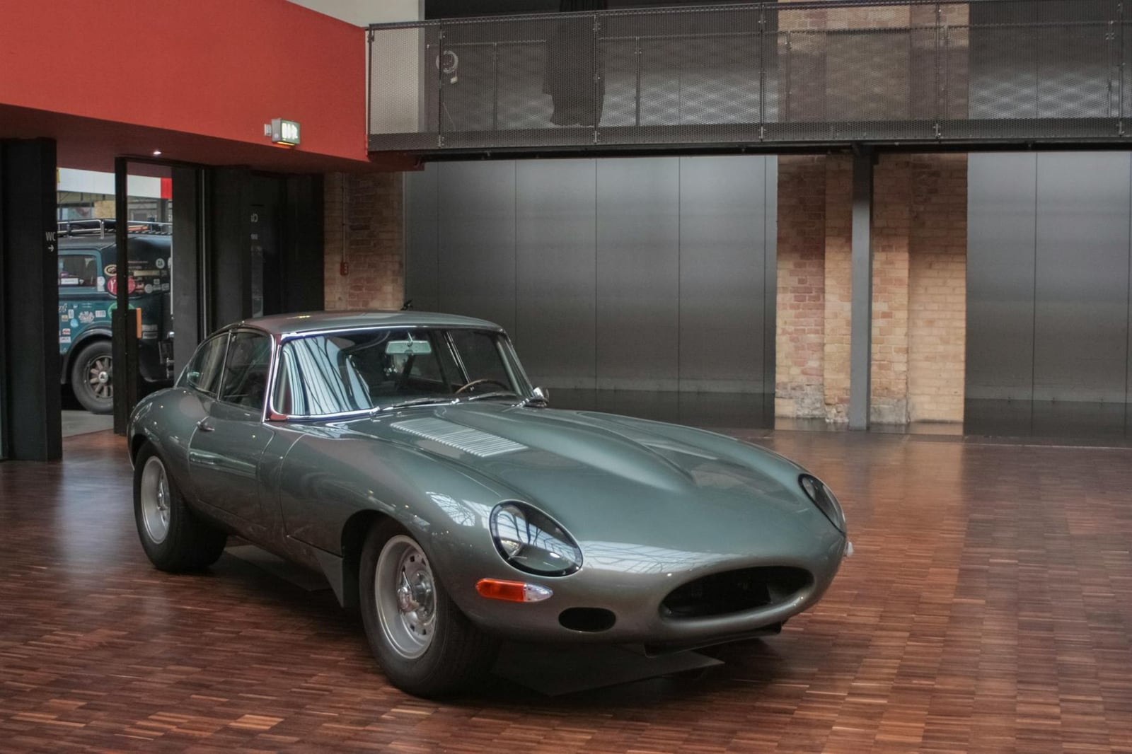 A silver-grey Jaguar E-Type Series 1 fixed-head coupe with covered headlamps, front three-quarter view in a museum hall