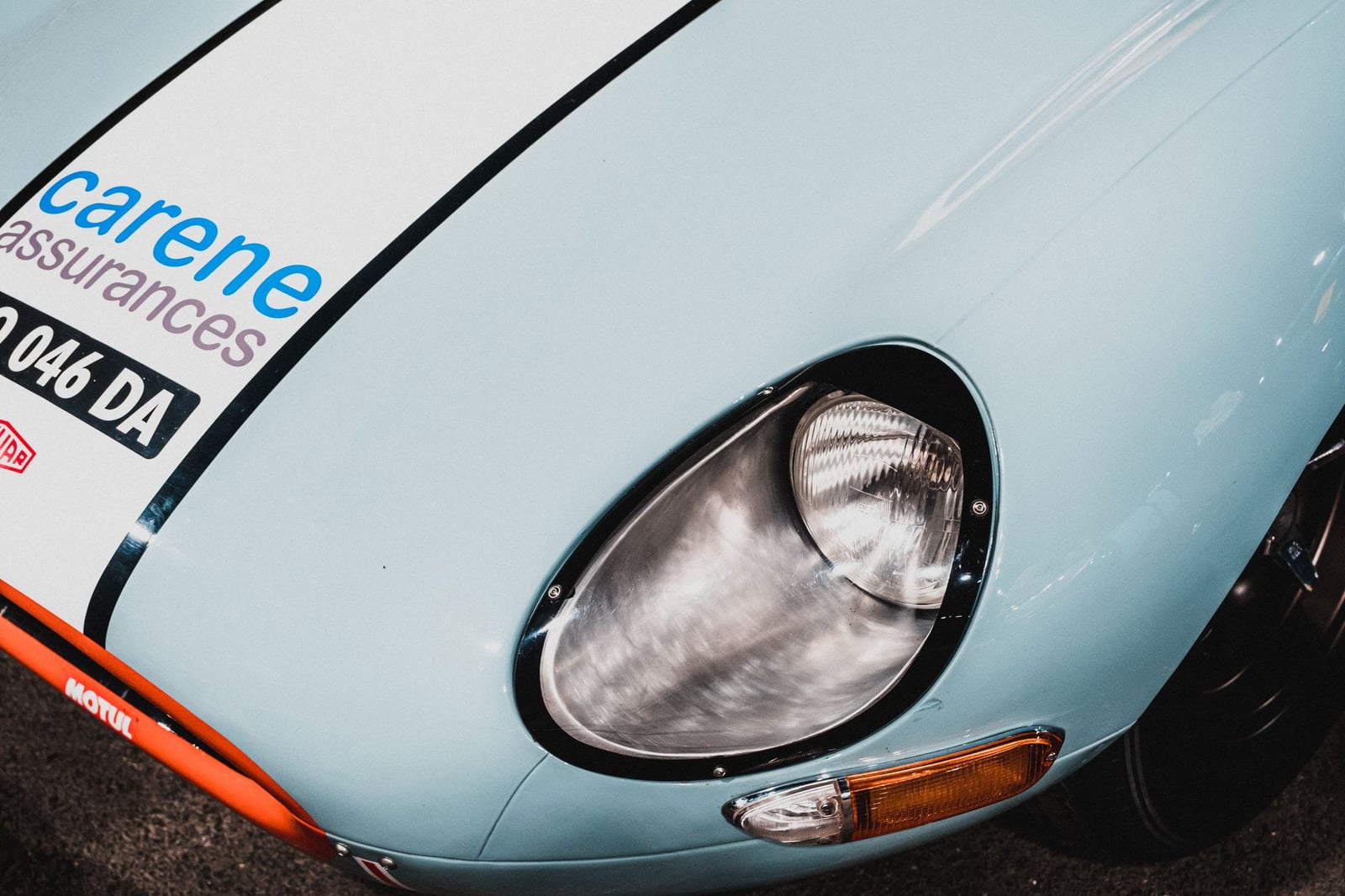 Close-up of the glass-covered headlamp faired into the wing of a pale blue Jaguar E-Type Series 1