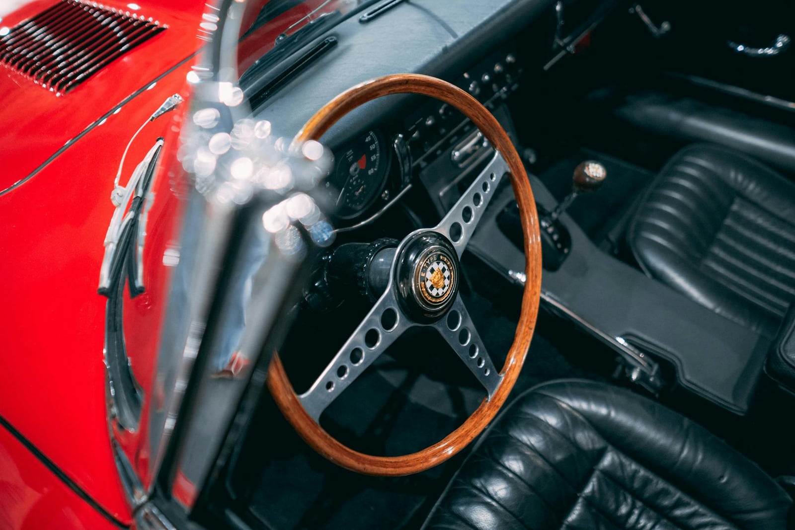 The interior of a Jaguar E-Type with a wood-rimmed steering wheel and a row of toggle switches