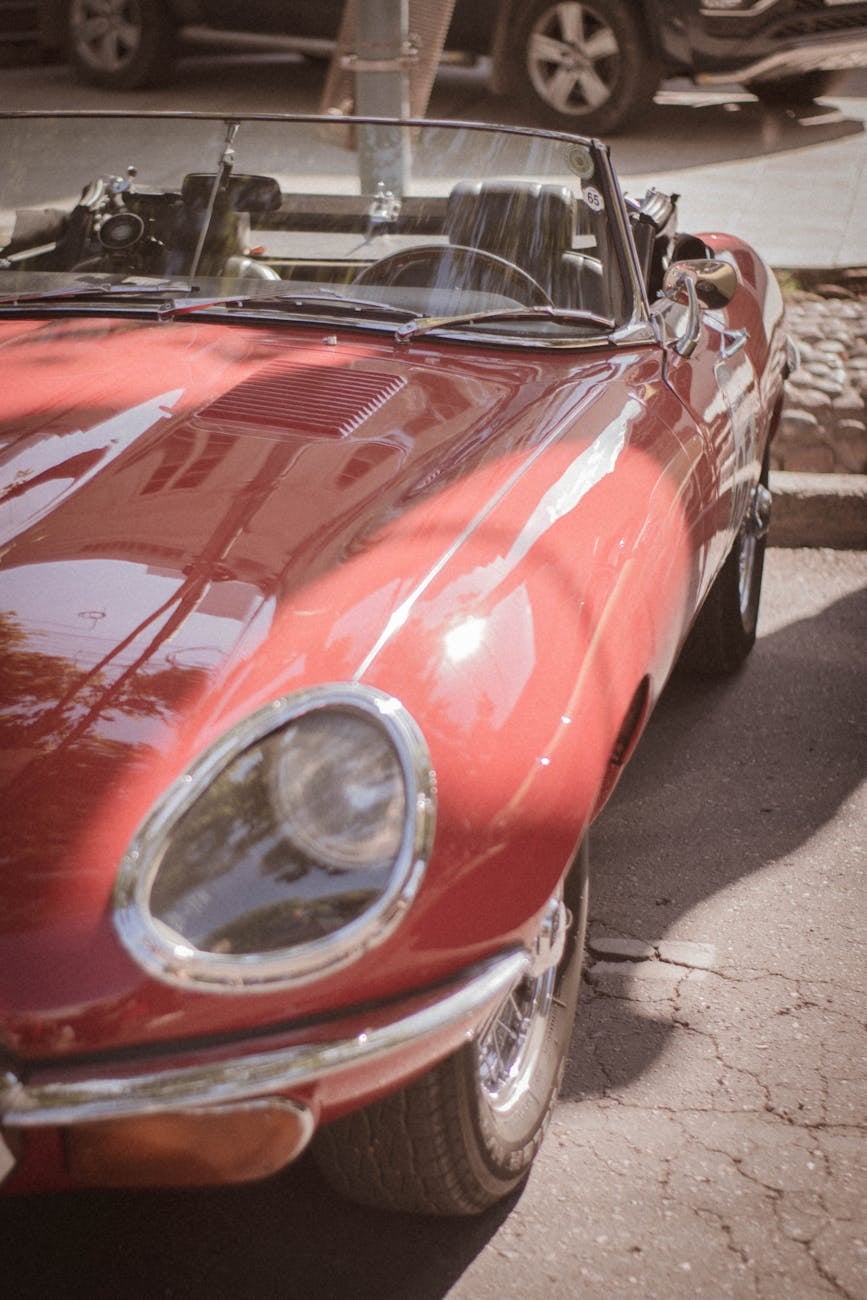 The open headlamp and front wing of a red Jaguar E-Type roadster