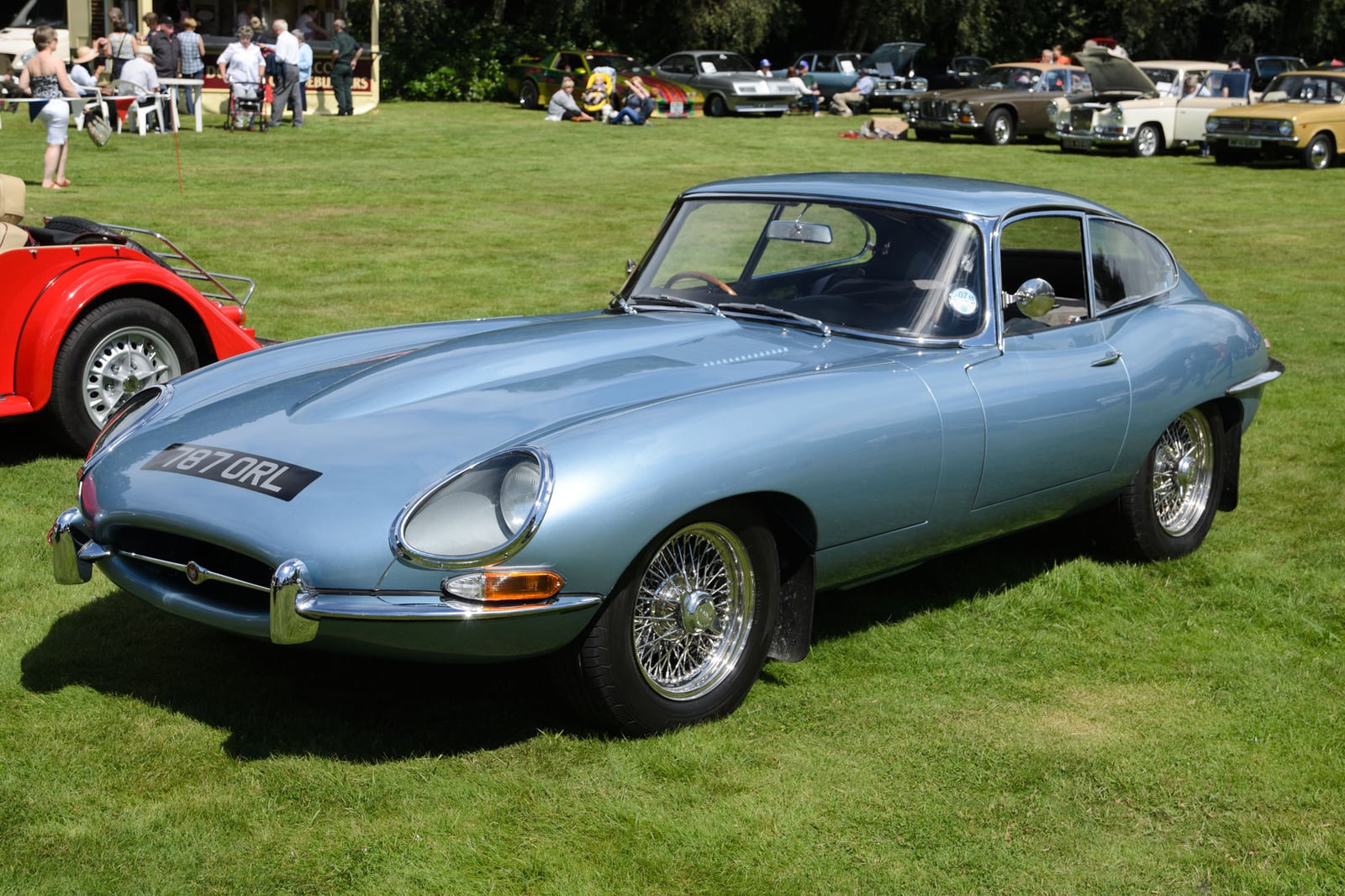 A light blue Jaguar E-Type Series 1 fixed-head coupe with covered headlamps at a show, front three-quarter view