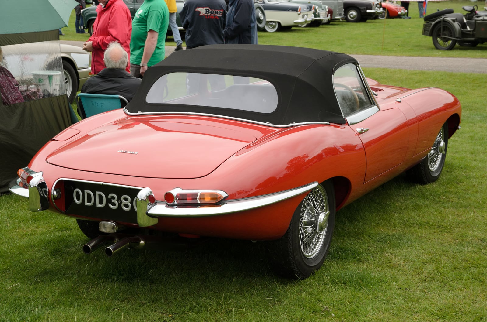 A red Jaguar E-Type Series 1 roadster with covered headlamps and the hood up, rear three-quarter view