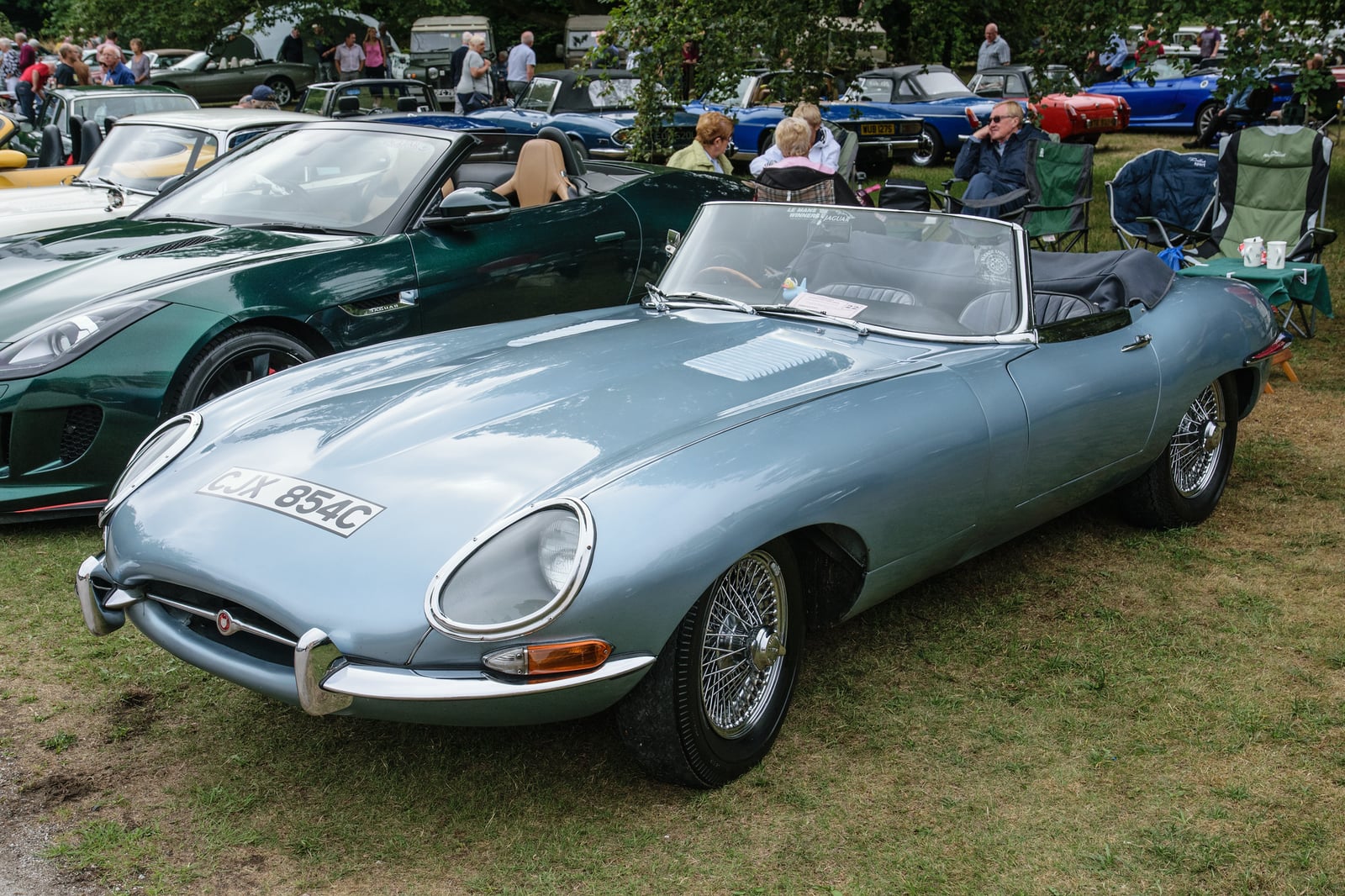 A light blue Jaguar E-Type Series 1 roadster with covered headlamps and the hood down, front three-quarter view