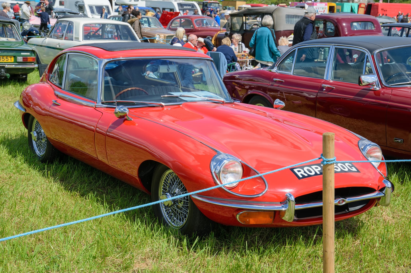 A red Jaguar E-Type Series 2 fixed-head coupe at a classic car show, front three-quarter view