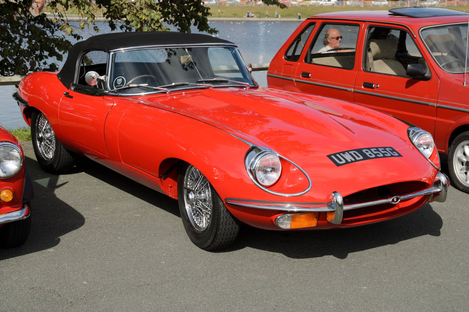 A red Jaguar E-Type Series 2 roadster with open headlamps at a classic car show, front three-quarter view