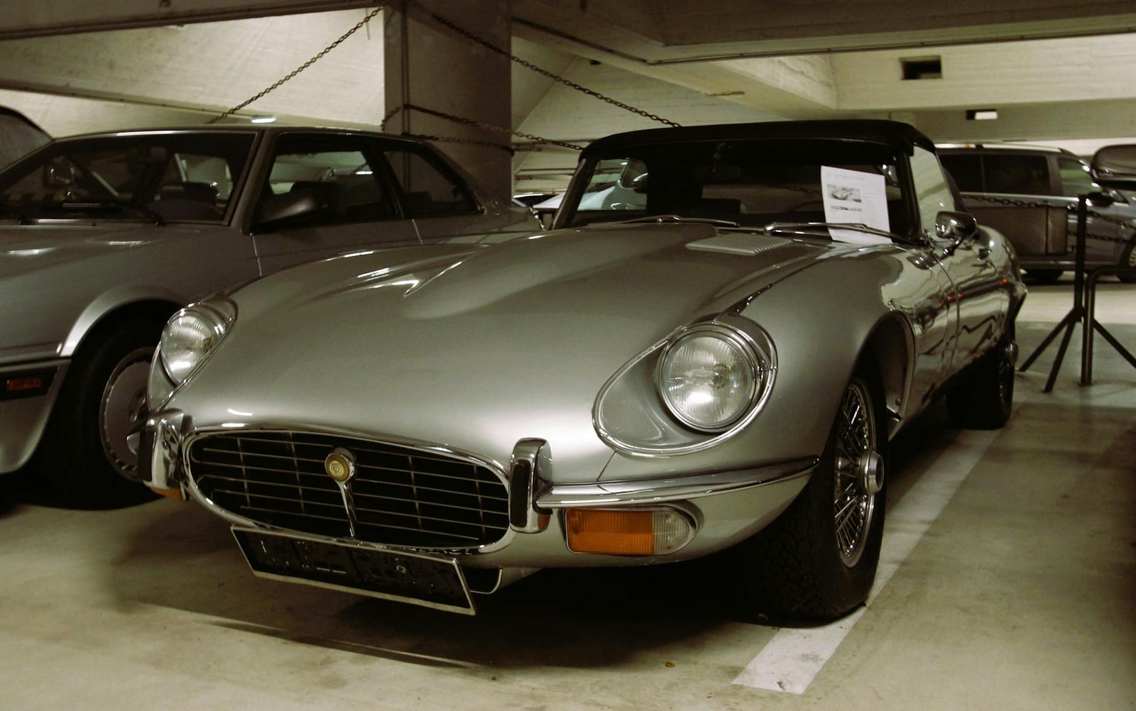 A silver Jaguar E-Type Series 3 V12 roadster with the hood up, front three-quarter view