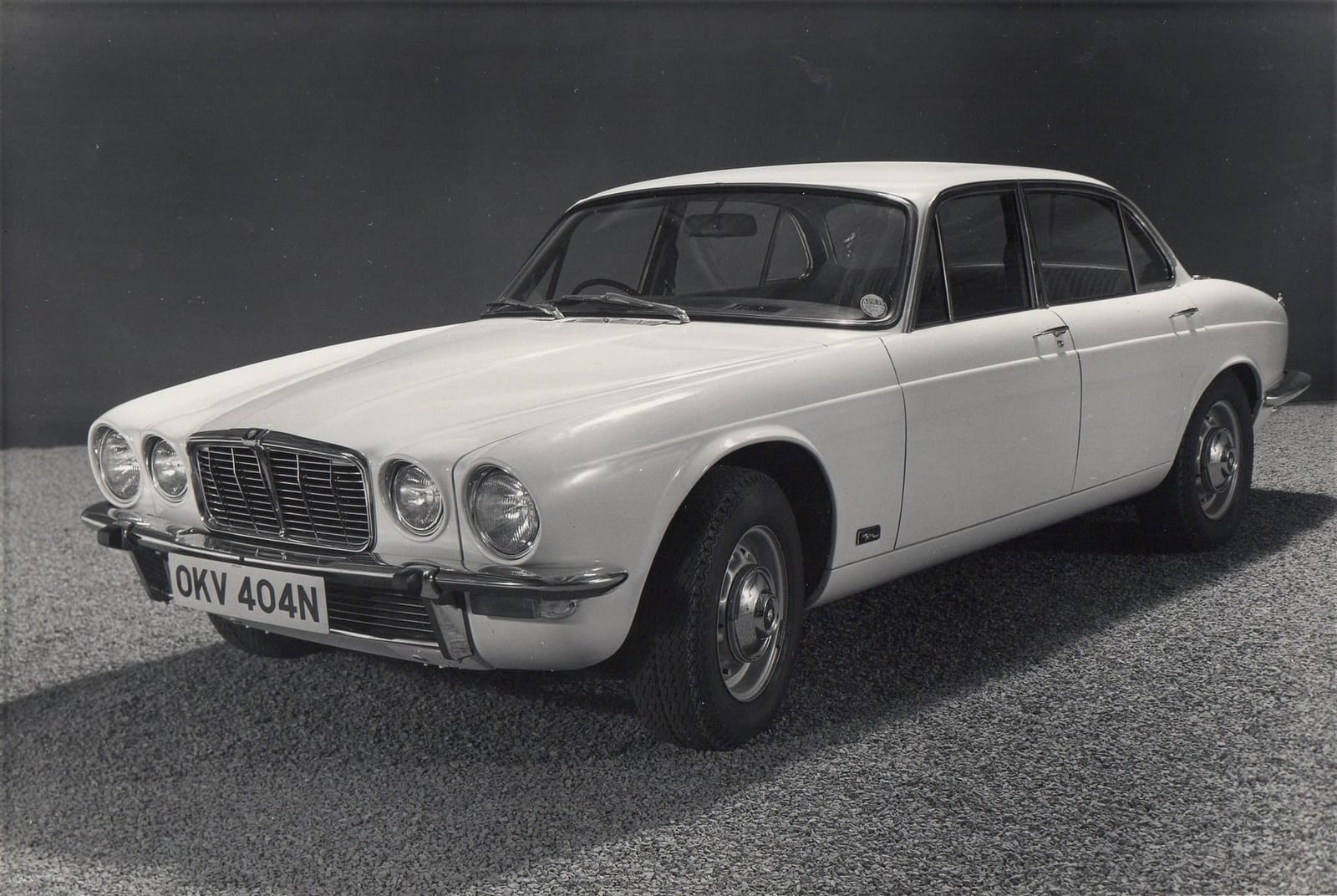 A period black and white photograph of a white 1975 Jaguar XJ 3.4 saloon with a UK registration
