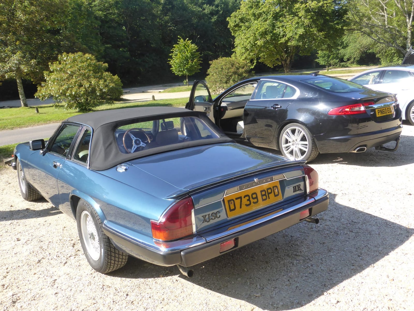 A blue 1987 Jaguar XJ-SC HE cabriolet with its targa roof panels fitted and a UK registration, parked on gravel