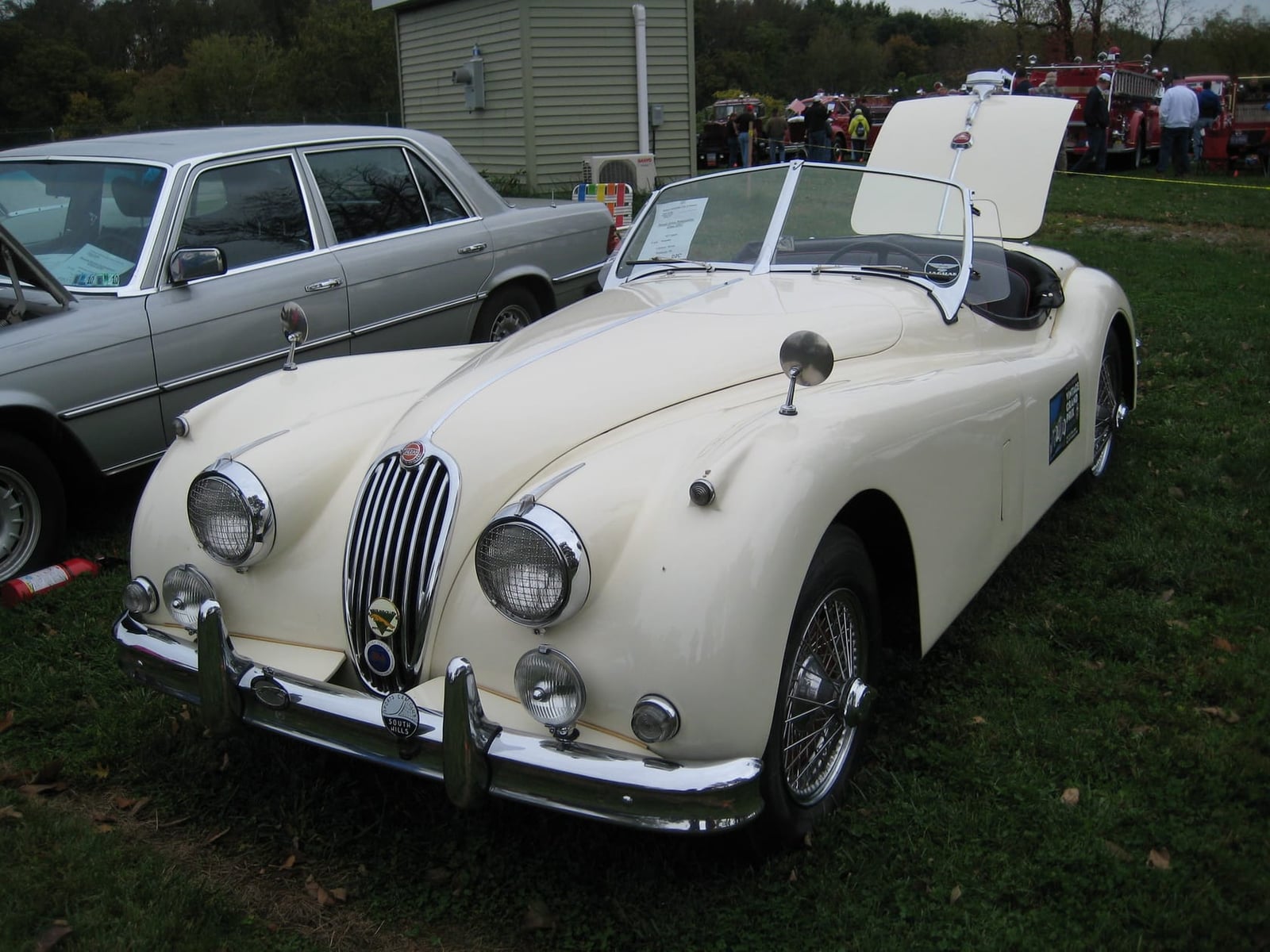 A cream Jaguar XK140 roadster with its bonnet raised at a classic car show