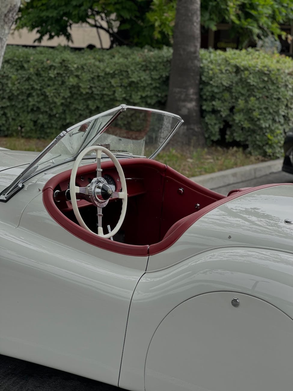 The cockpit and rear wing of a white Jaguar XK120 roadster with a red interior