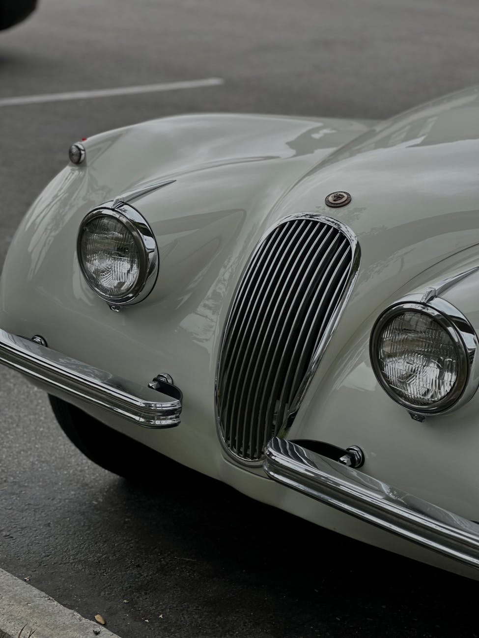 Close-up of a white Jaguar XK120 front showing the slim chrome grille and faired headlamps