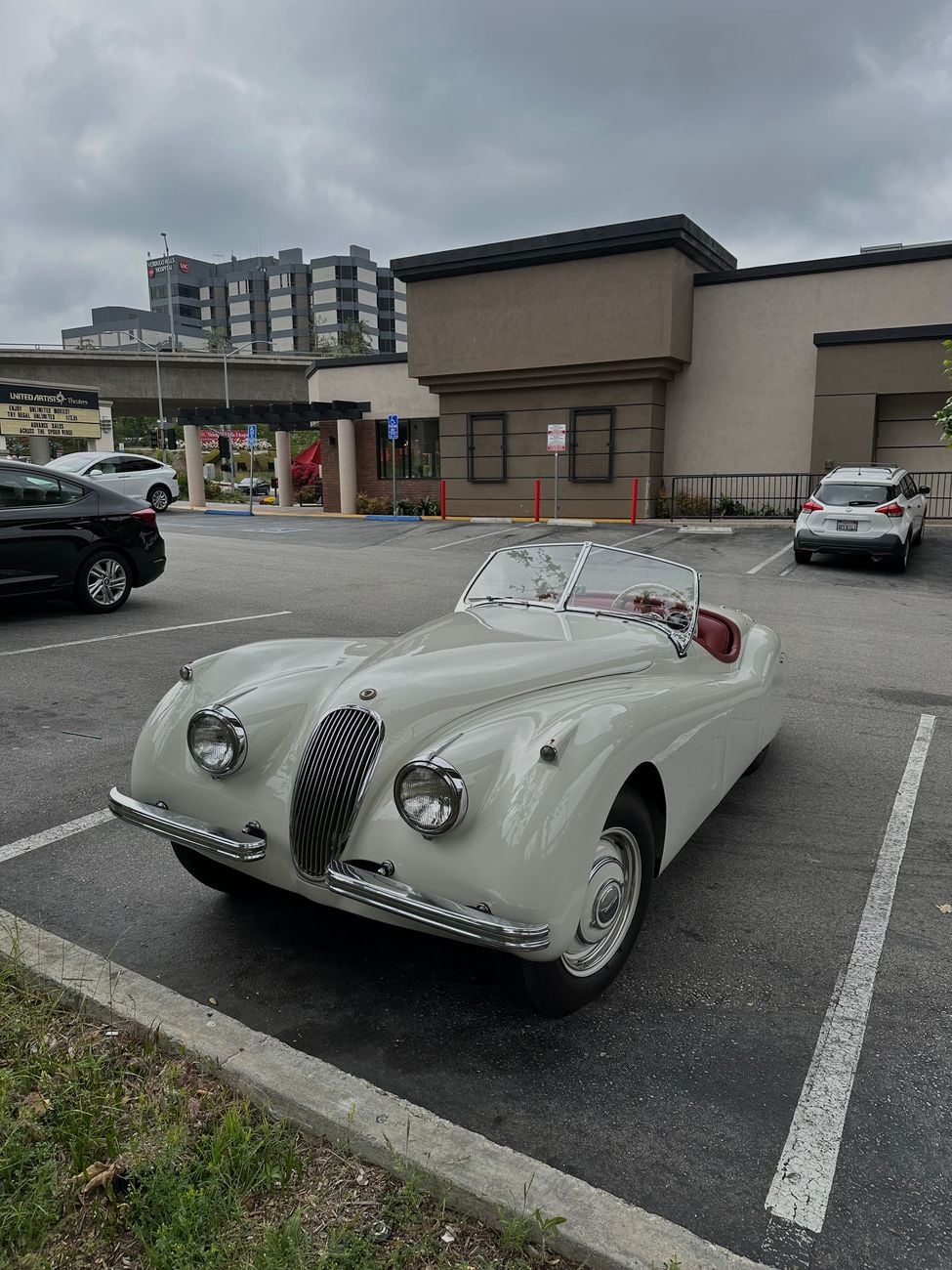 A white Jaguar XK120 roadster in a car park, front three-quarter view