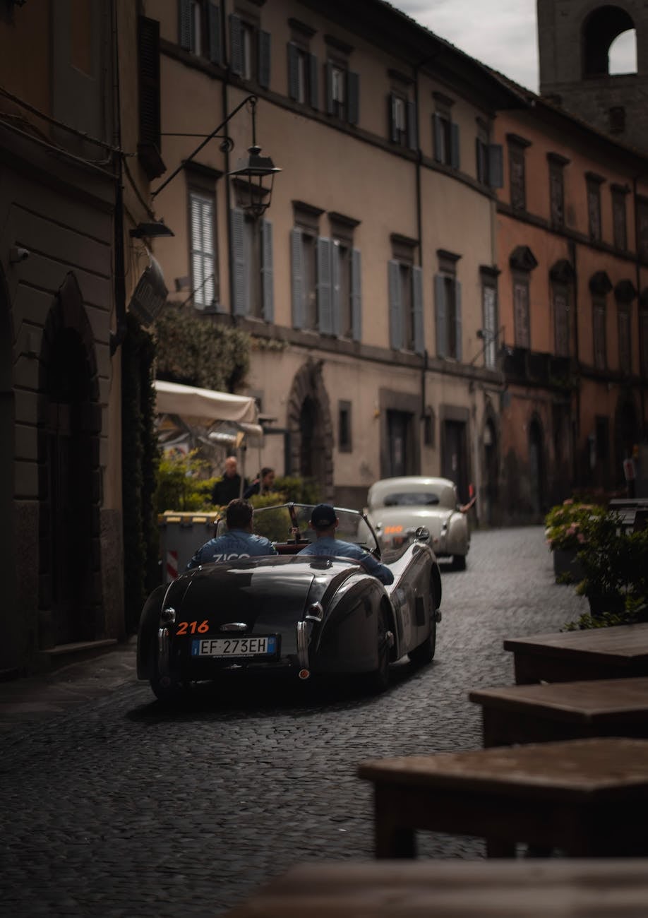 A dark Jaguar XK120 roadster driving through a cobbled town on a historic road rally