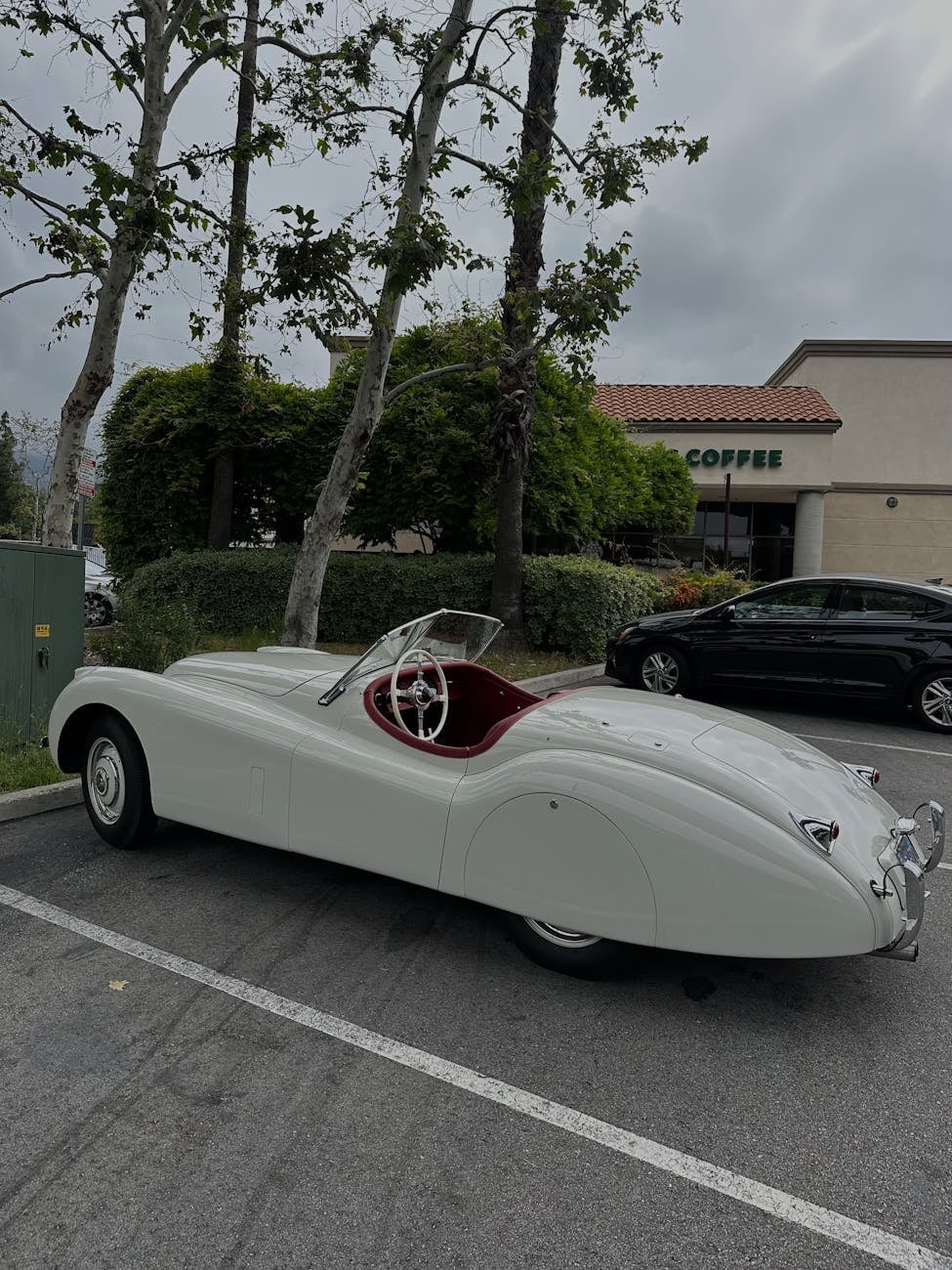 A white Jaguar XK120 roadster seen from the rear three-quarter, with red cockpit and wire wheels