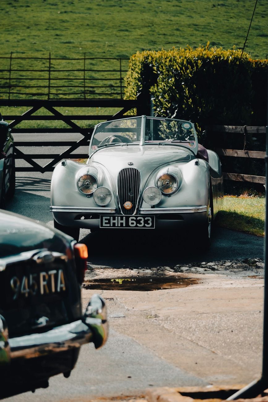 A silver Jaguar XK120 roadster parked by a stone wall, front three-quarter view