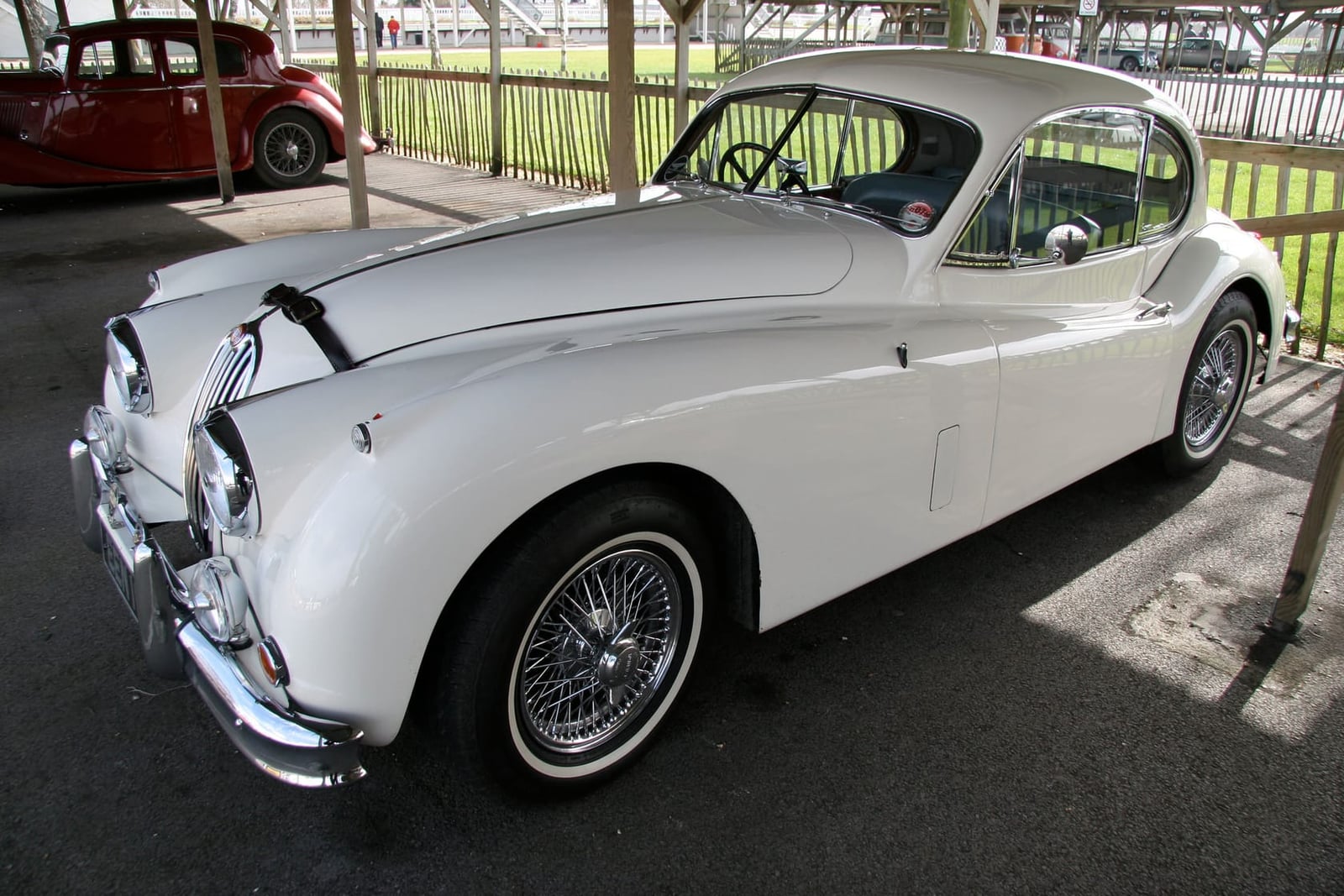 A white Jaguar XK140 fixed-head coupe parked on tarmac, side view