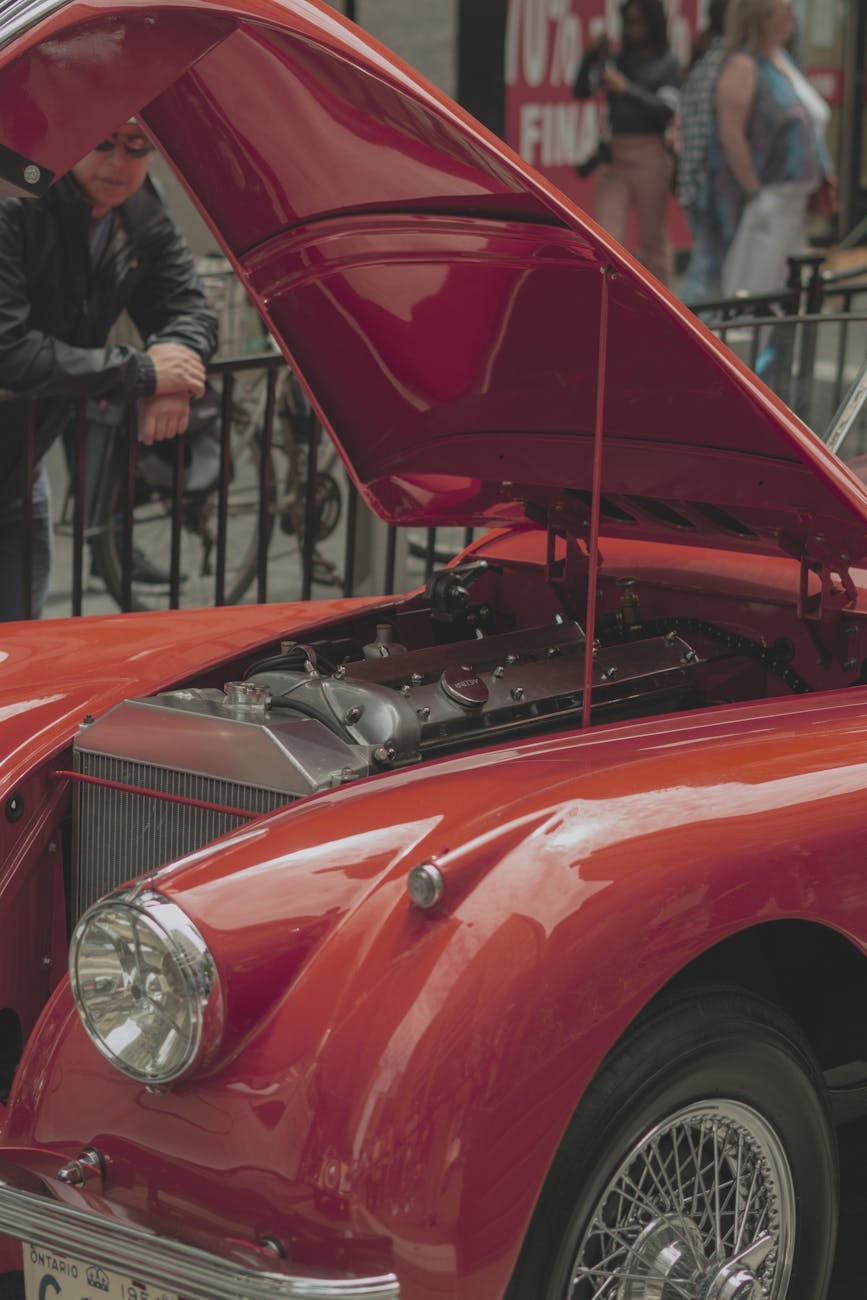 A red Jaguar XK140 with its bonnet open showing the XK twin-cam engine