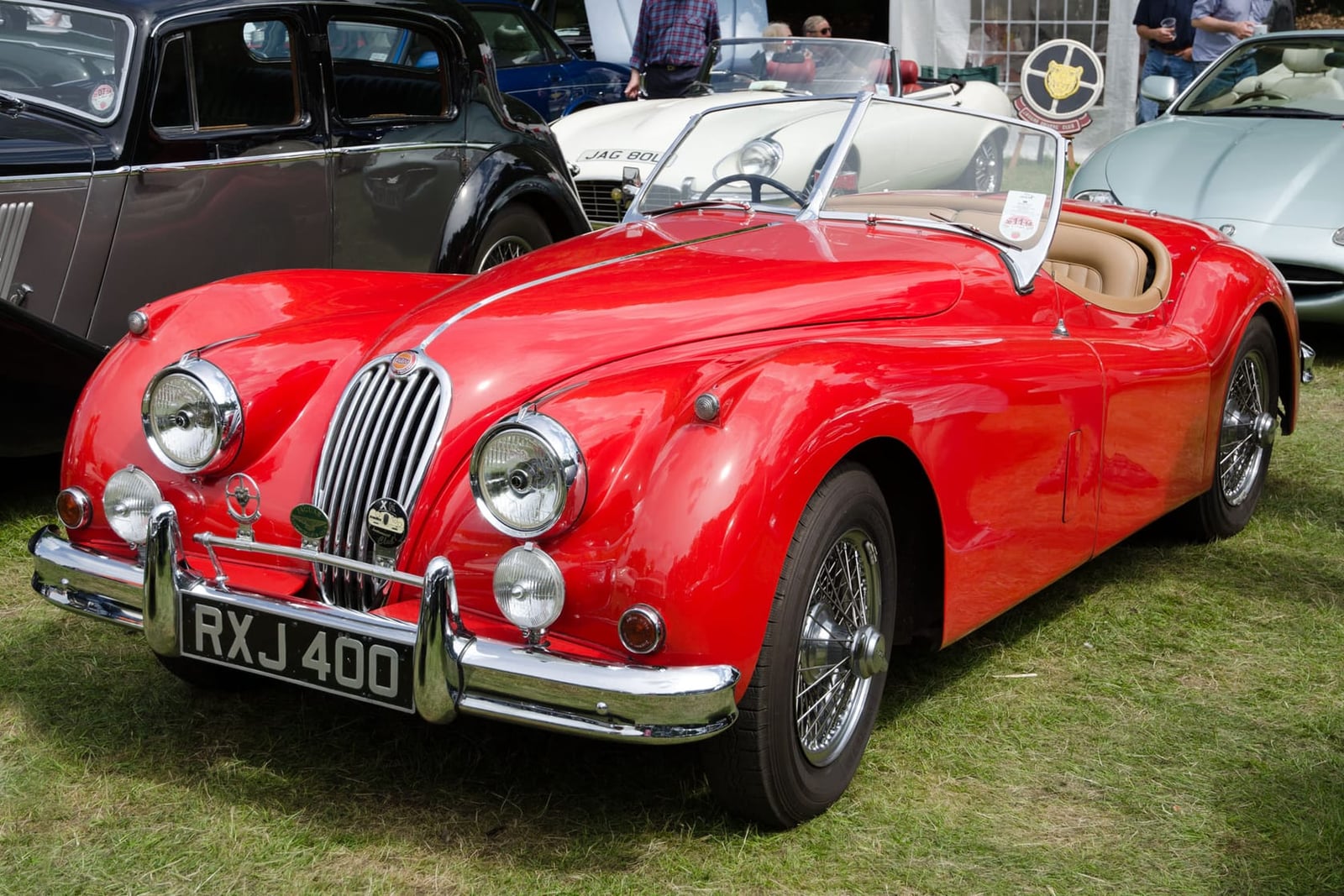 A red 1955 Jaguar XK140 roadster with its windscreen folded and a UK registration on a show field