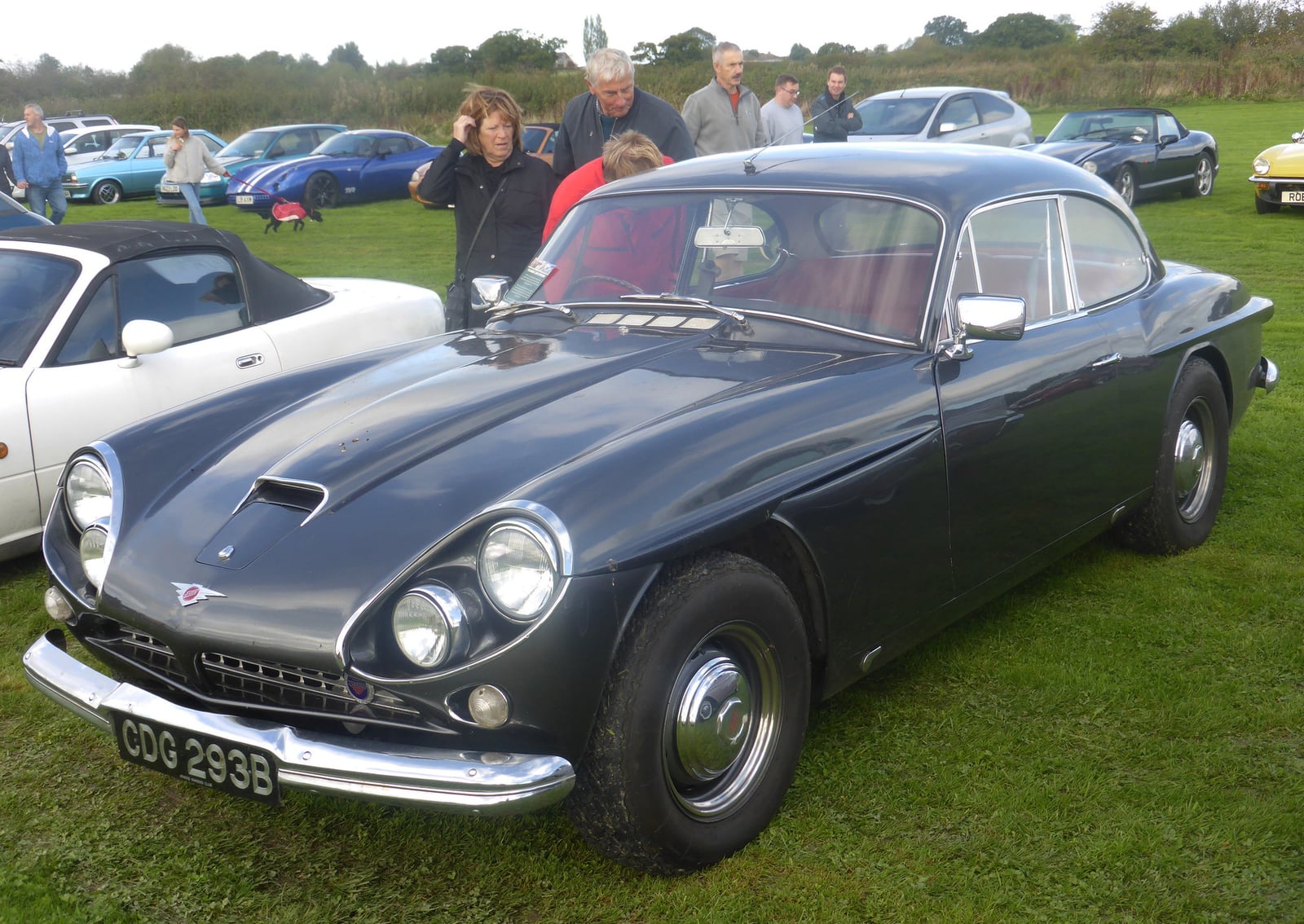 A light blue Jensen CV8 on grass at a show, front three-quarter view