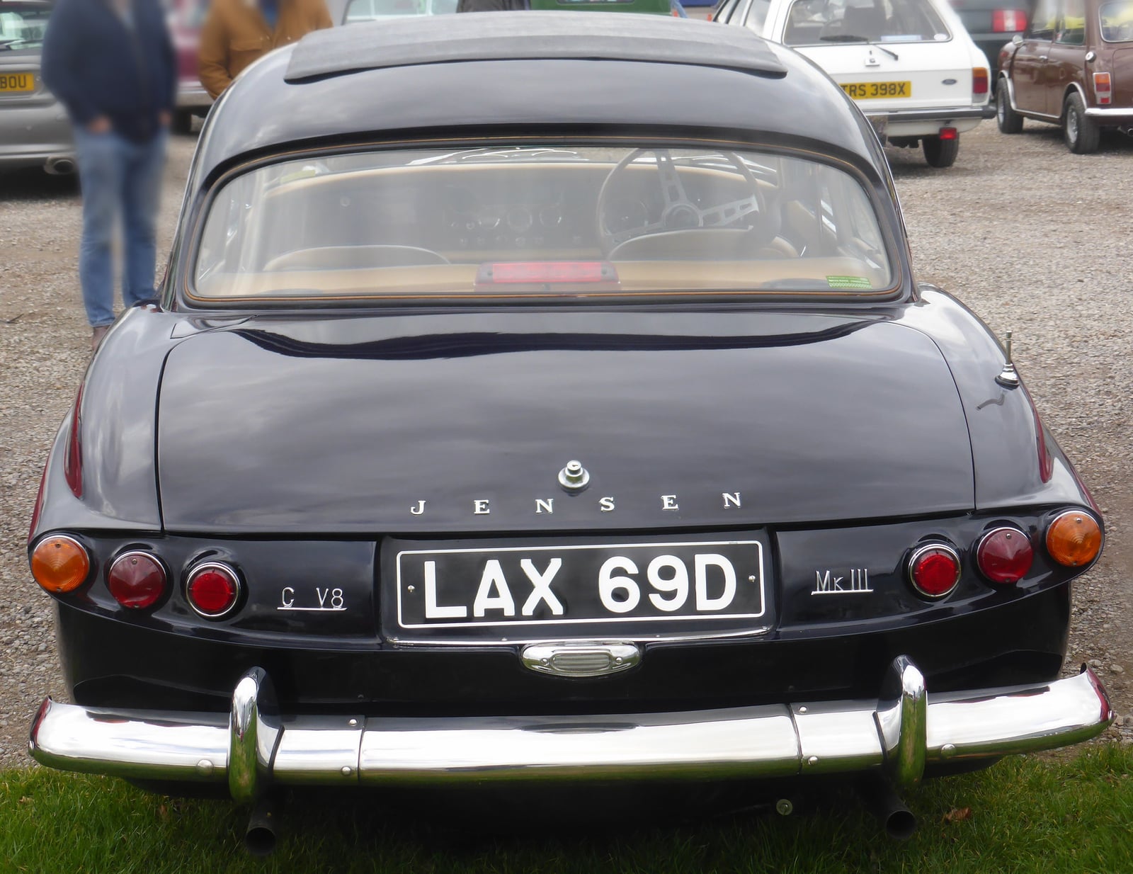The rear of a dark Jensen CV8 Mk III on grass, UK registration LAX 69D