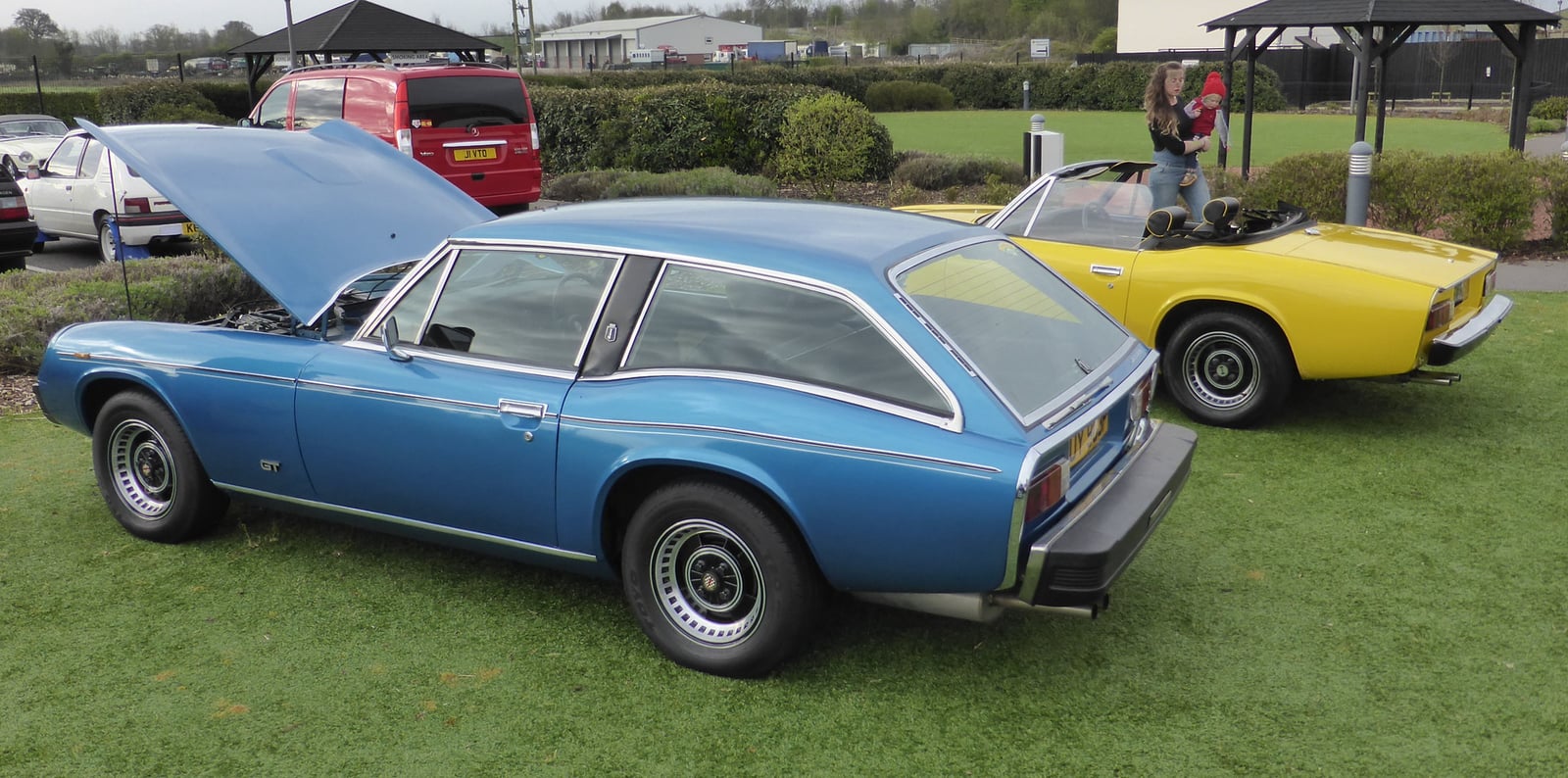 A blue Jensen GT shooting-brake beside a yellow Jensen-Healey roadster at a show