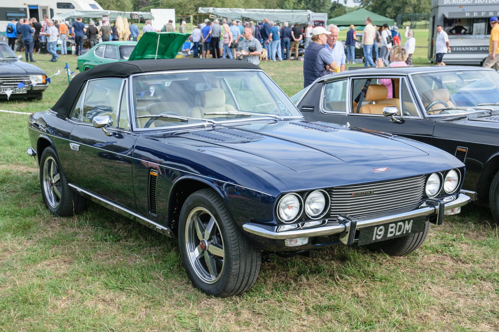 A dark blue Jensen Interceptor convertible at a show, front three-quarter view, UK registration 19 BDM