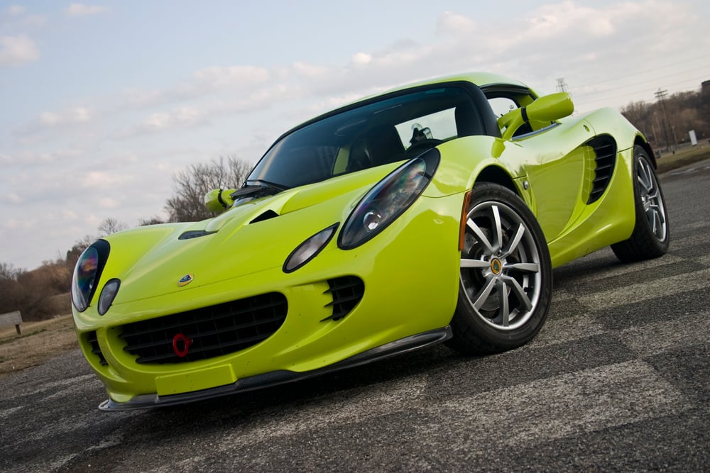 A bright lime-green Lotus Elise Series 1 roadster, front three-quarter view on a tarmac apron