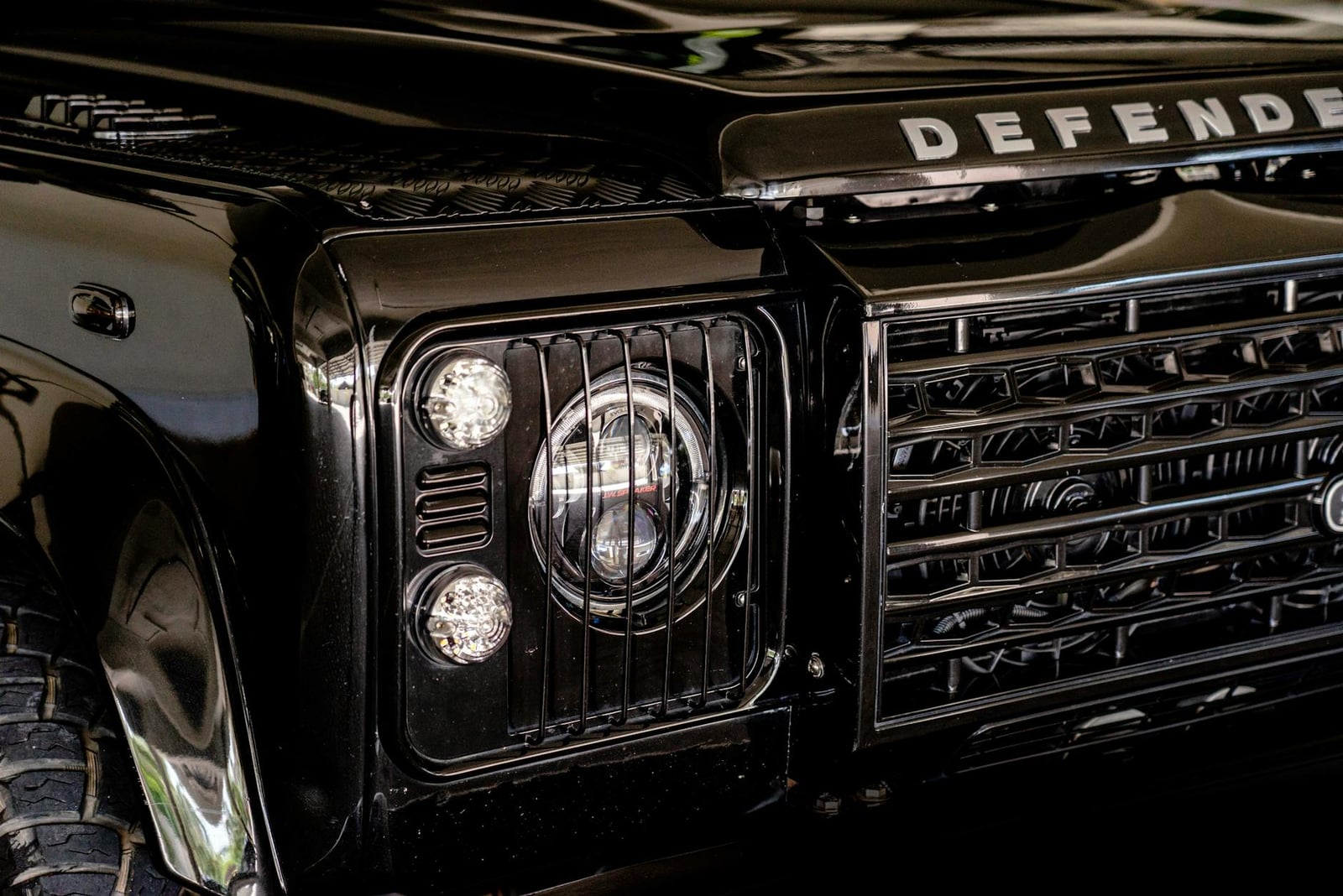 Close-up of the round headlamps and grille of a black Land Rover Defender