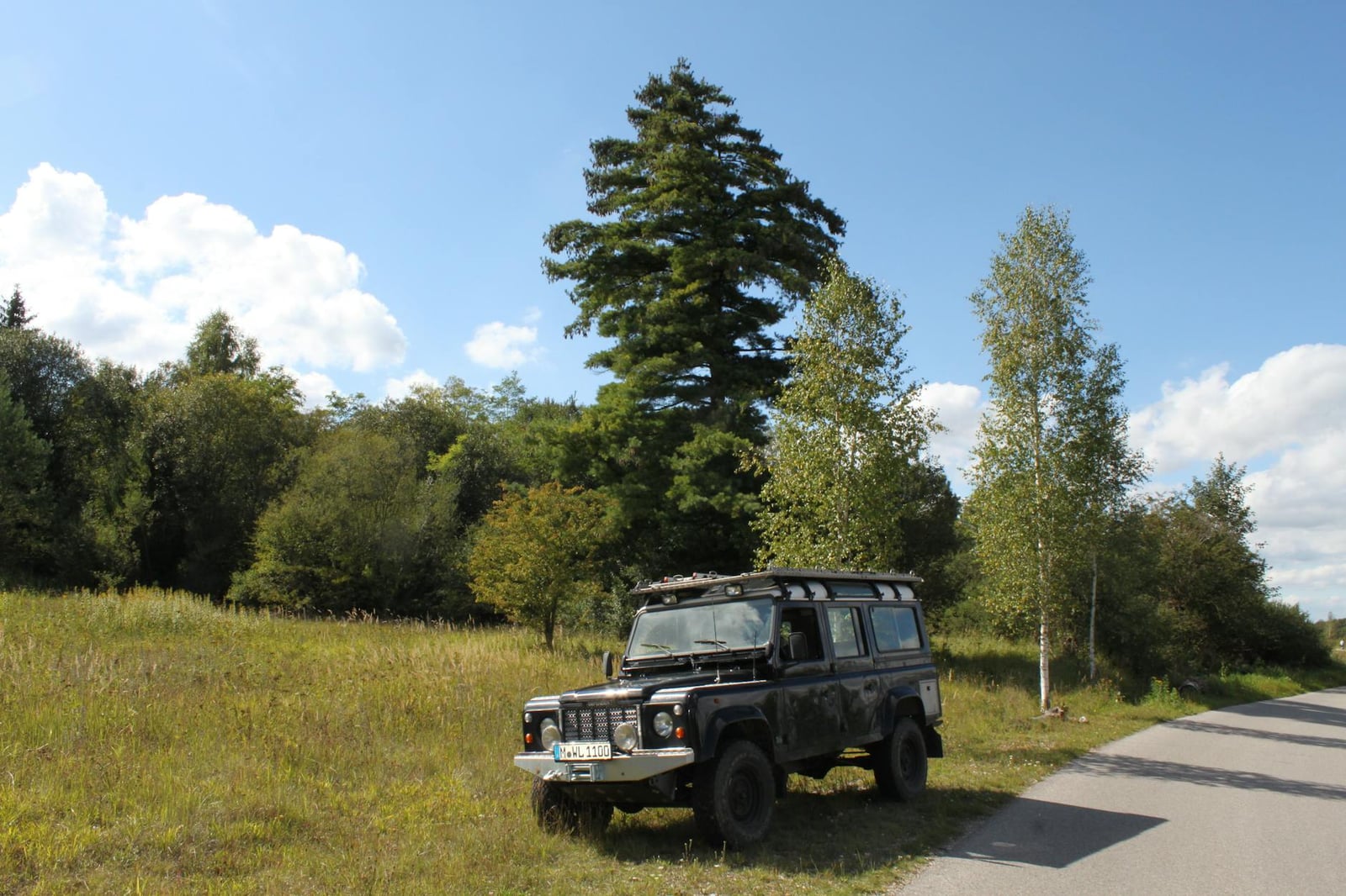 A dark long-wheelbase Land Rover Defender 110 parked by trees in the countryside