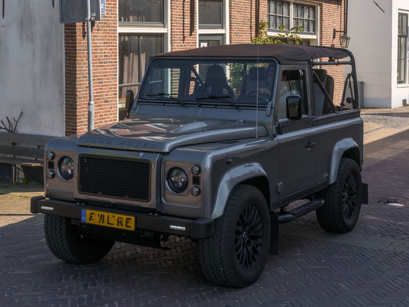 A silver short-wheelbase Land Rover Defender 90 on a cobbled street with a UK number plate