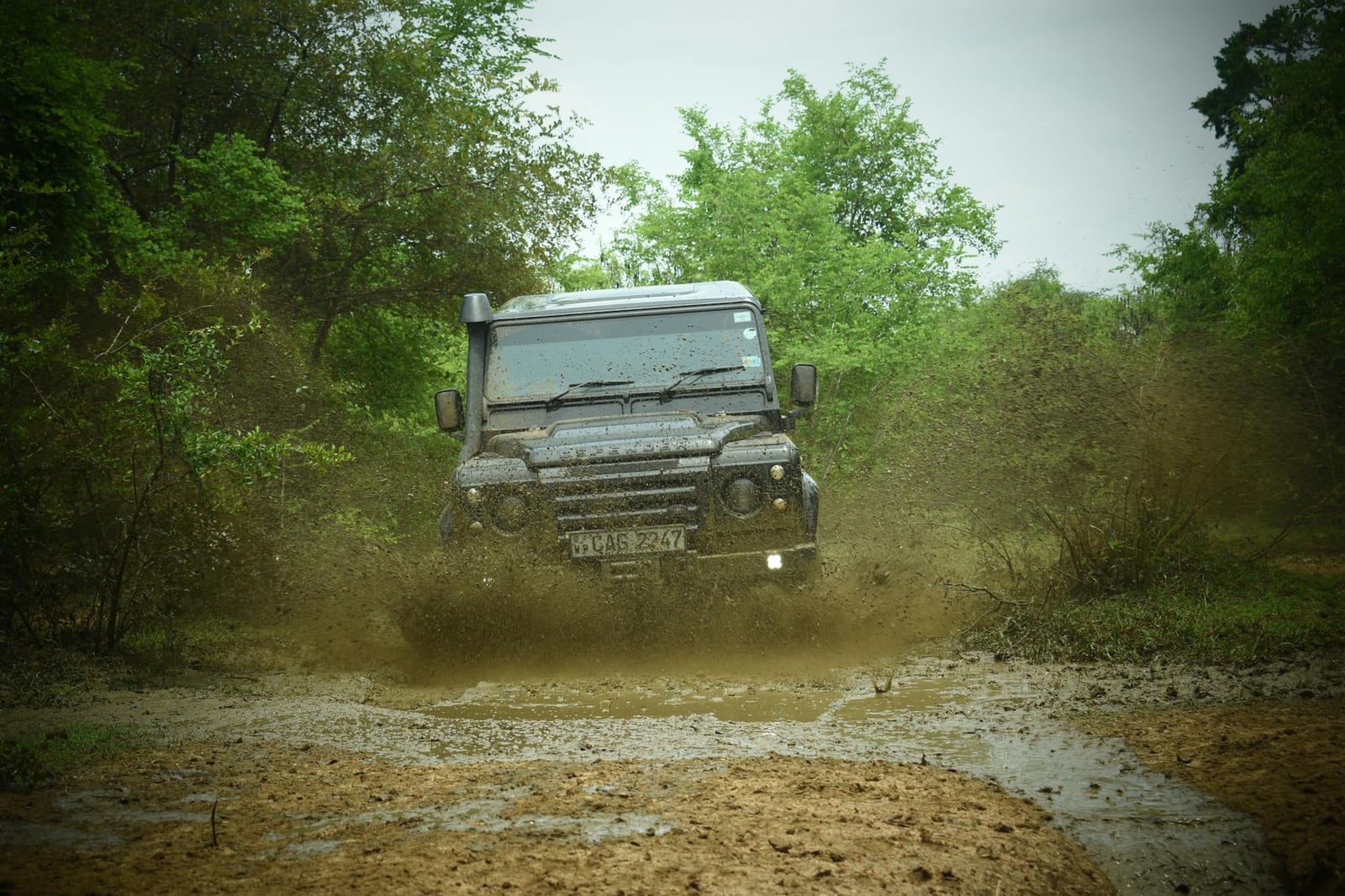 A Land Rover Defender splashing through a muddy forest track