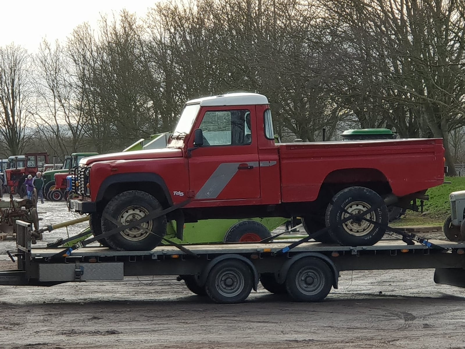 A red 1999 Land Rover Defender 110 Td5 pick-up strapped to a trailer at an outdoor sale