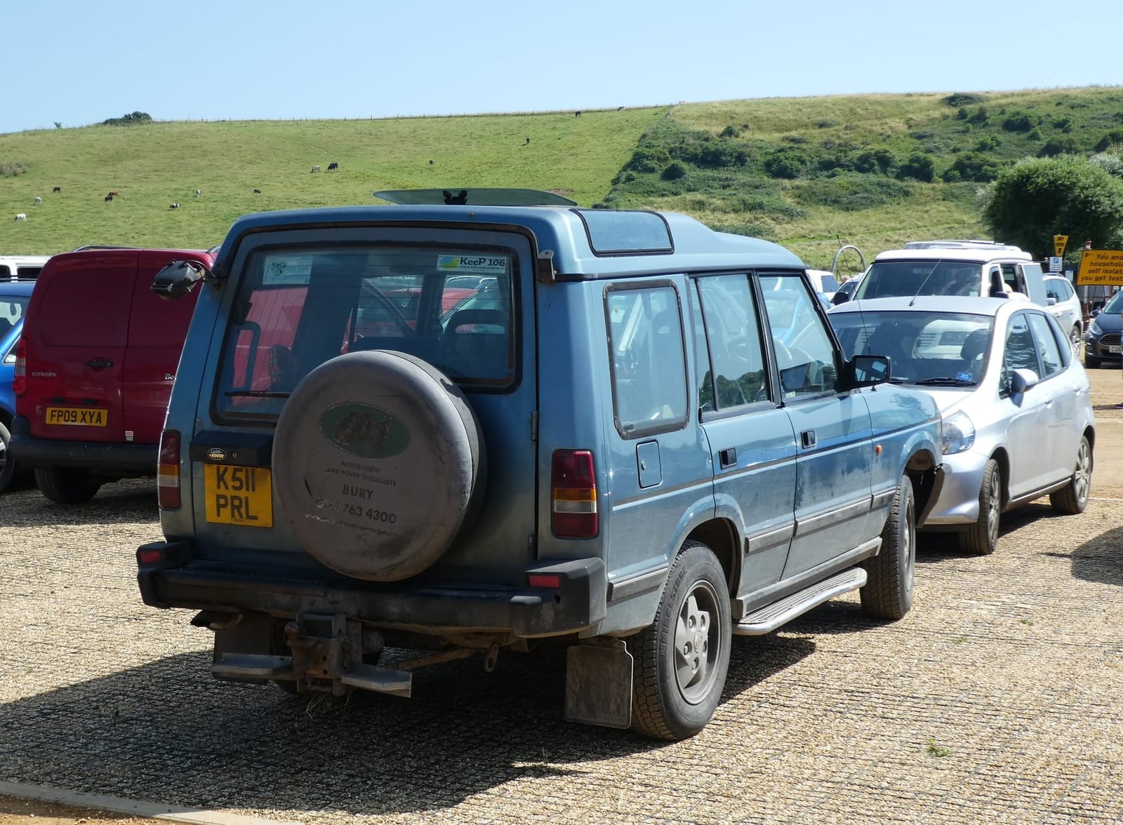 A blue 1993 Land Rover Discovery parked above a coastal bay, rear three-quarter view