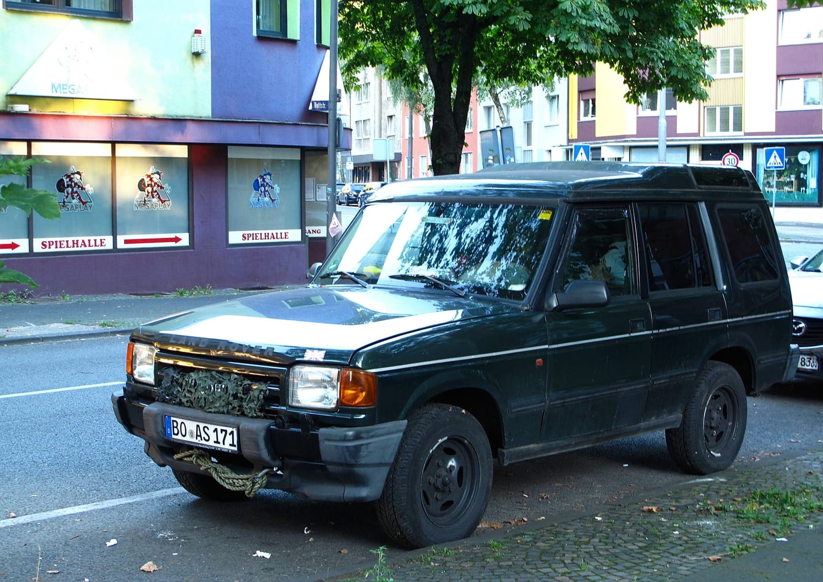 A dark green Land Rover Discovery 1 parked on grass at a vehicle gathering, front three-quarter view
