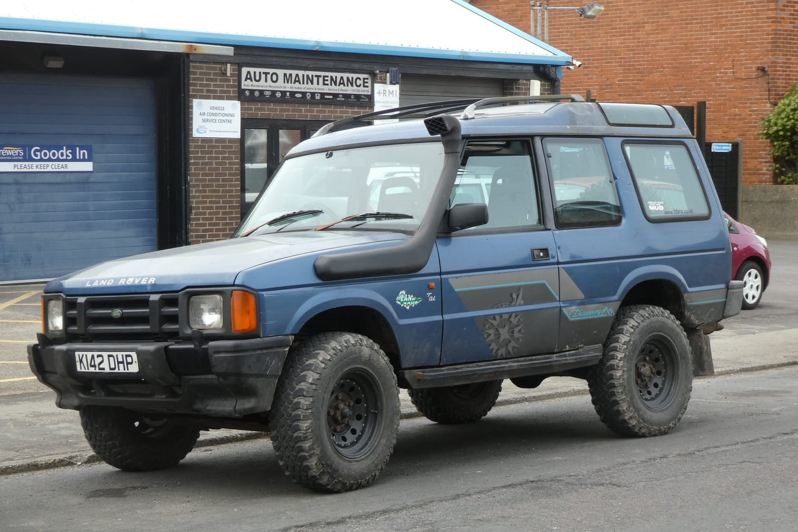 A blue 1992 three-door Land Rover Discovery Tdi with off-road tyres and a snorkel outside a garage workshop