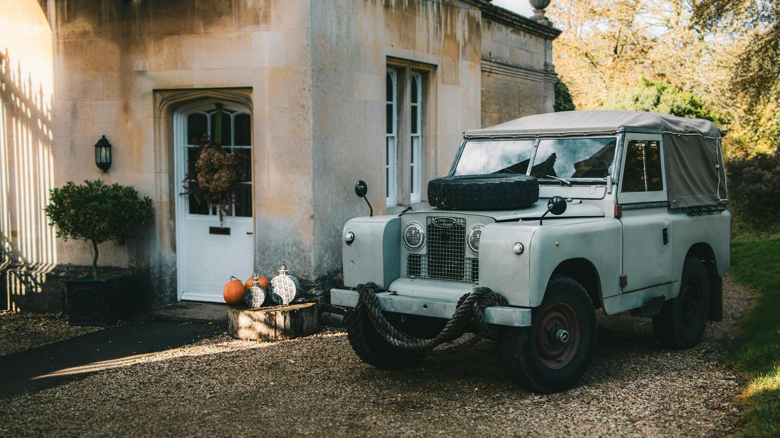 A Land Rover Series II with a canvas tilt parked outside a stone house