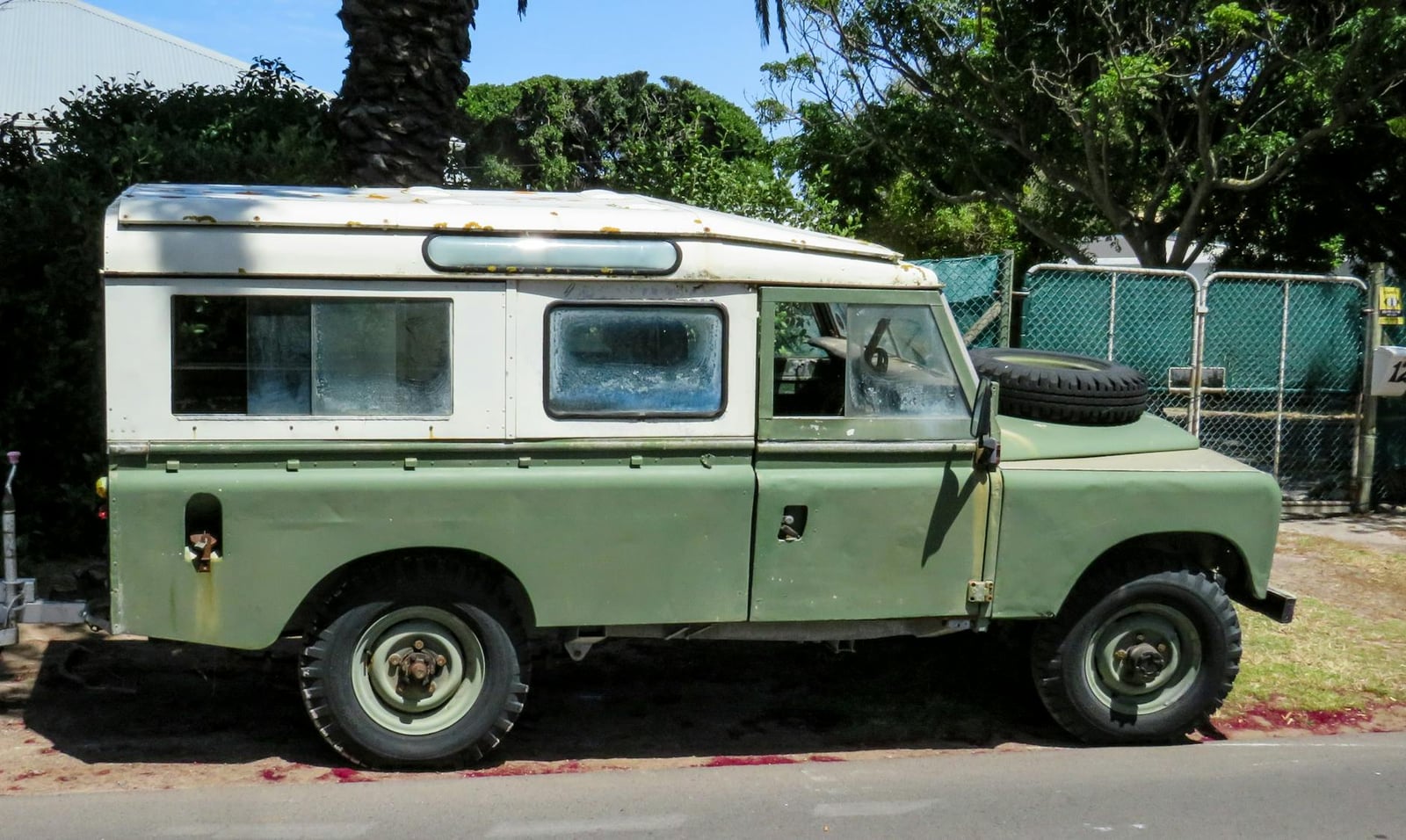 A green Land Rover Series station wagon parked under trees
