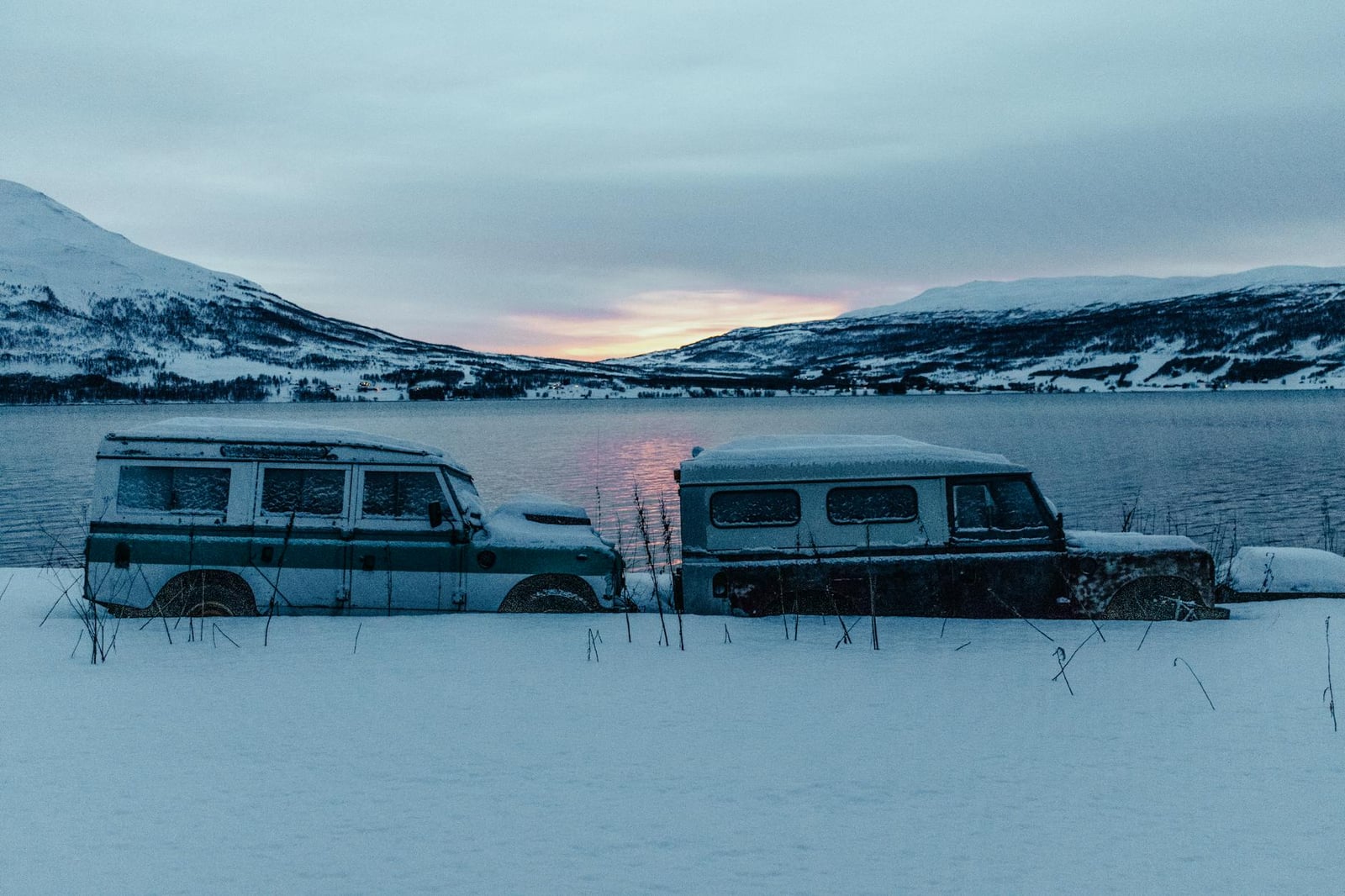 Two classic Land Rover Series station wagons in snow beside a frozen lake