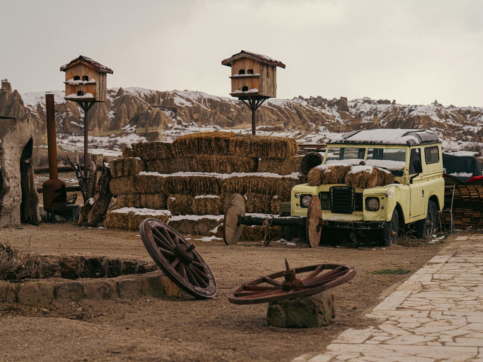 A yellow Land Rover Series III parked among hay bales in a wintry yard