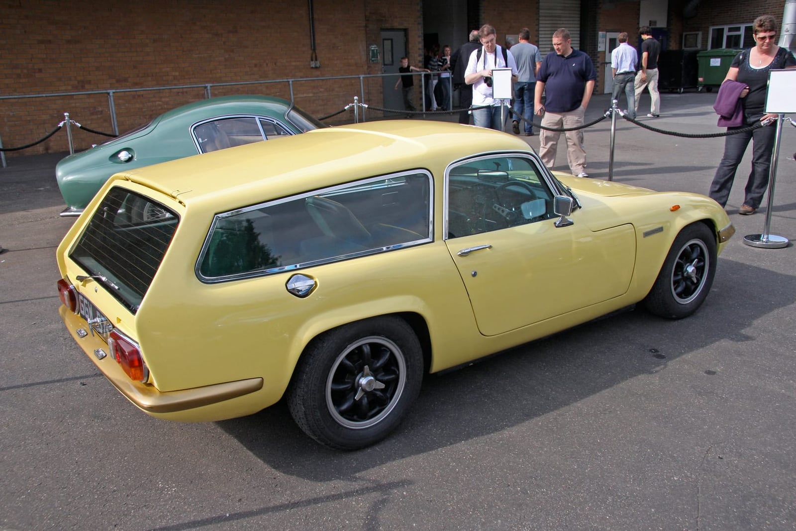 A yellow Lotus Elan estate conversion parked on tarmac, rear three-quarter view