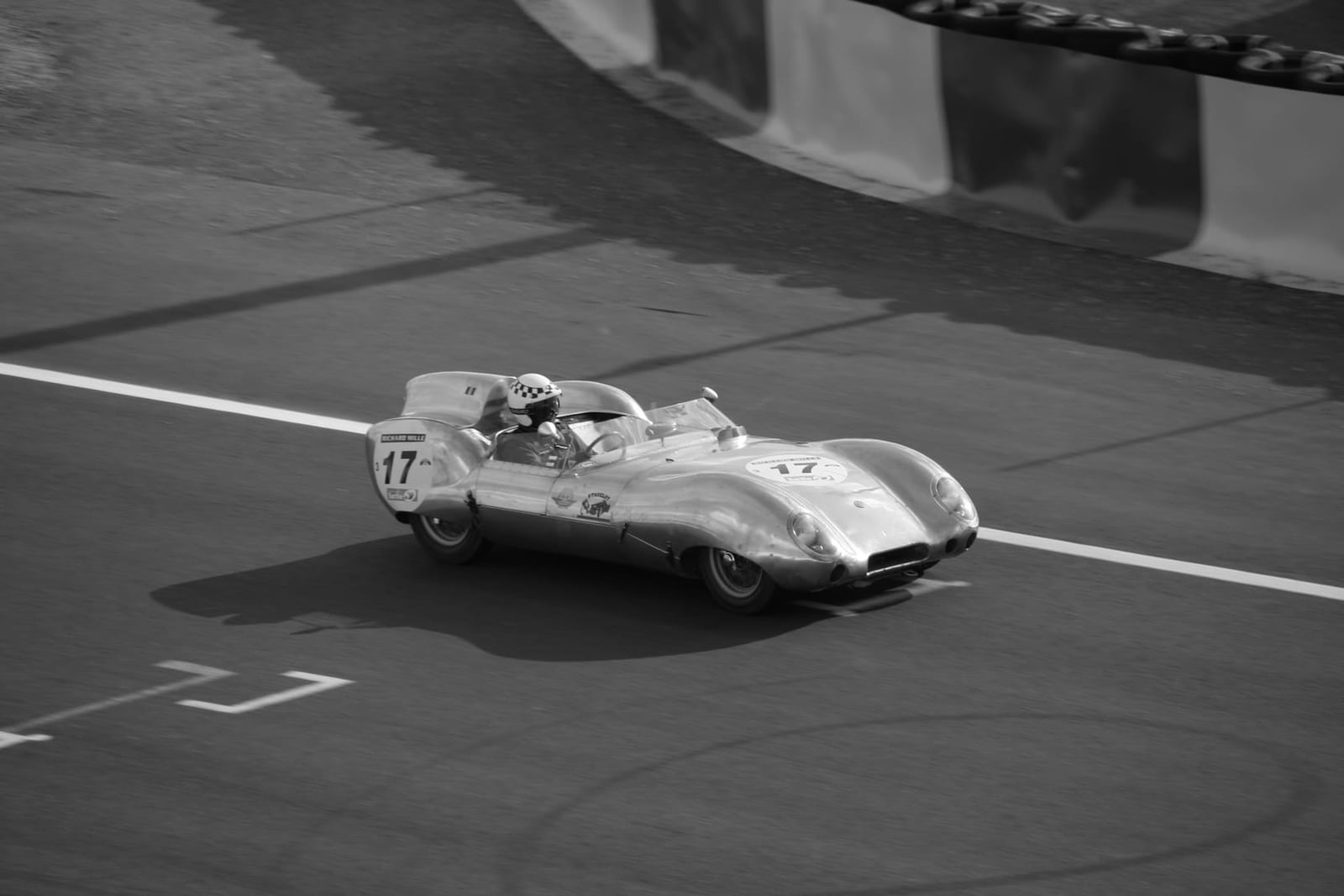 A black and white photograph of a Lotus Eleven carrying race number 17 at speed on a circuit