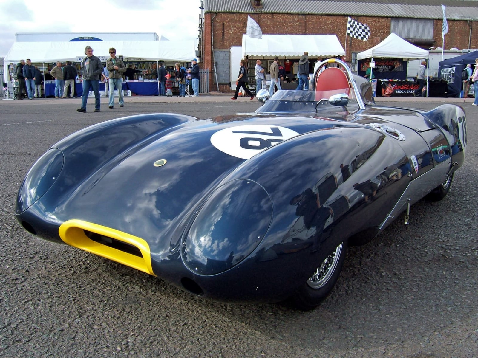 A dark blue Lotus Eleven Le Mans carrying race number 76 in a circuit paddock