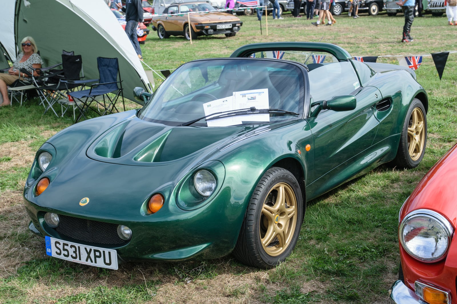 A British racing green Lotus Elise Series 1 with gold wheels, three-quarter front view at a classic-car show