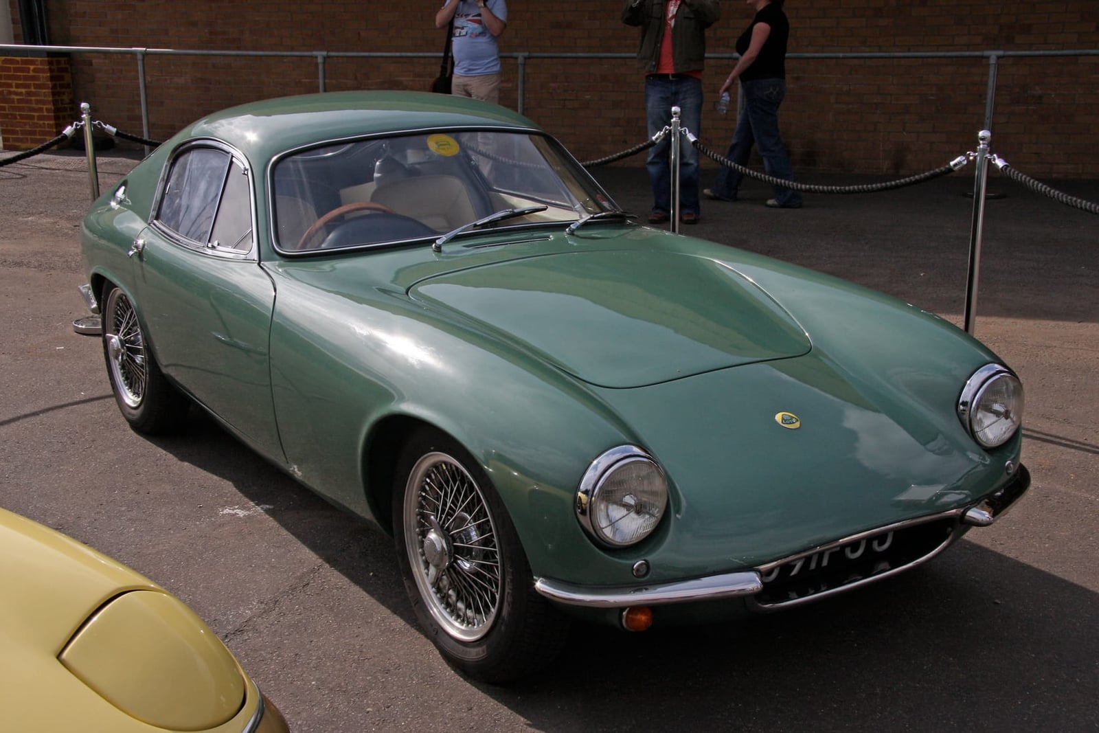 A green Lotus Elite on wire wheels parked on tarmac at a classic car event, front three-quarter view