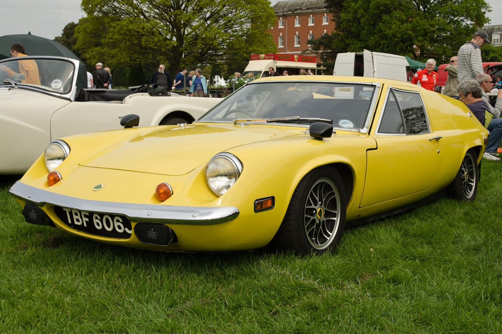 A yellow Lotus Europa on grass at a classic car show, front three-quarter view, UK registration TBF 606J