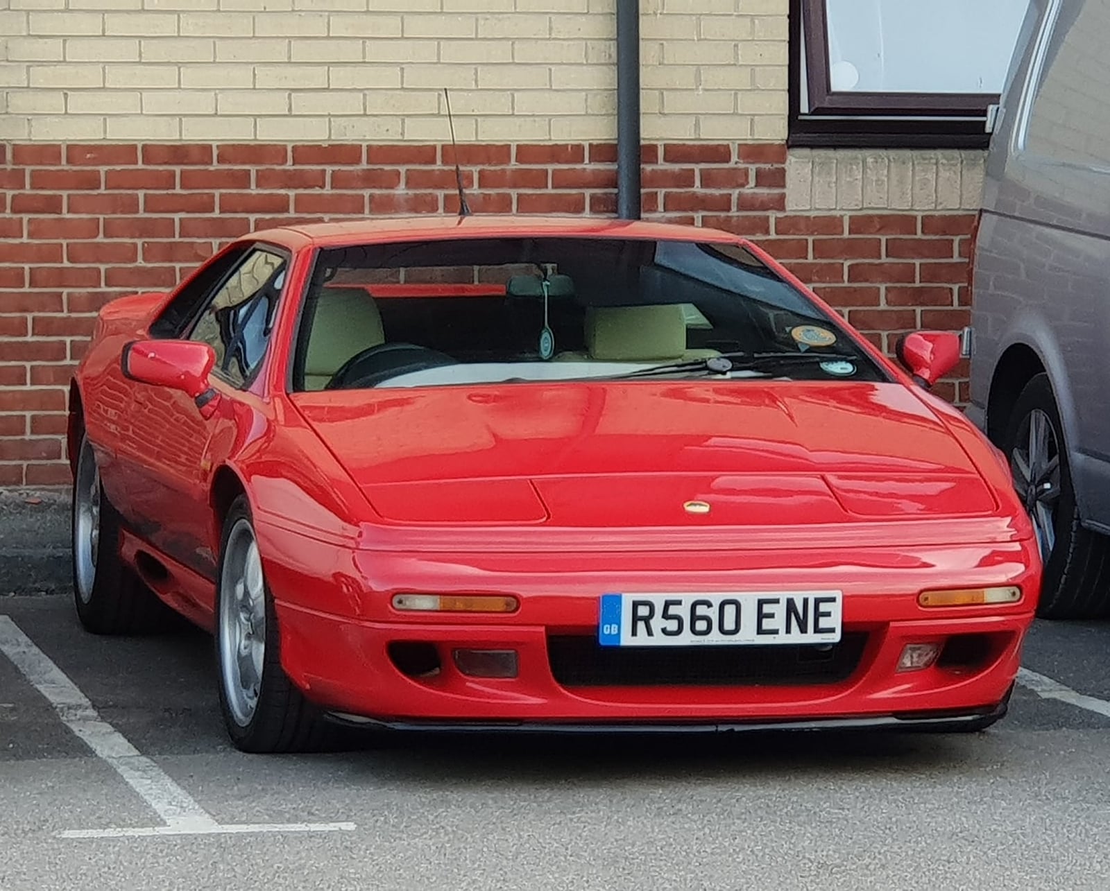 A red 1998 Lotus Esprit V8 with a UK registration parked against a brick wall