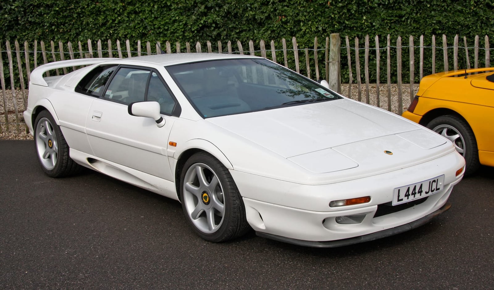 A white Lotus Esprit S4 parked beside a fence, side view, UK registration L444 JCL